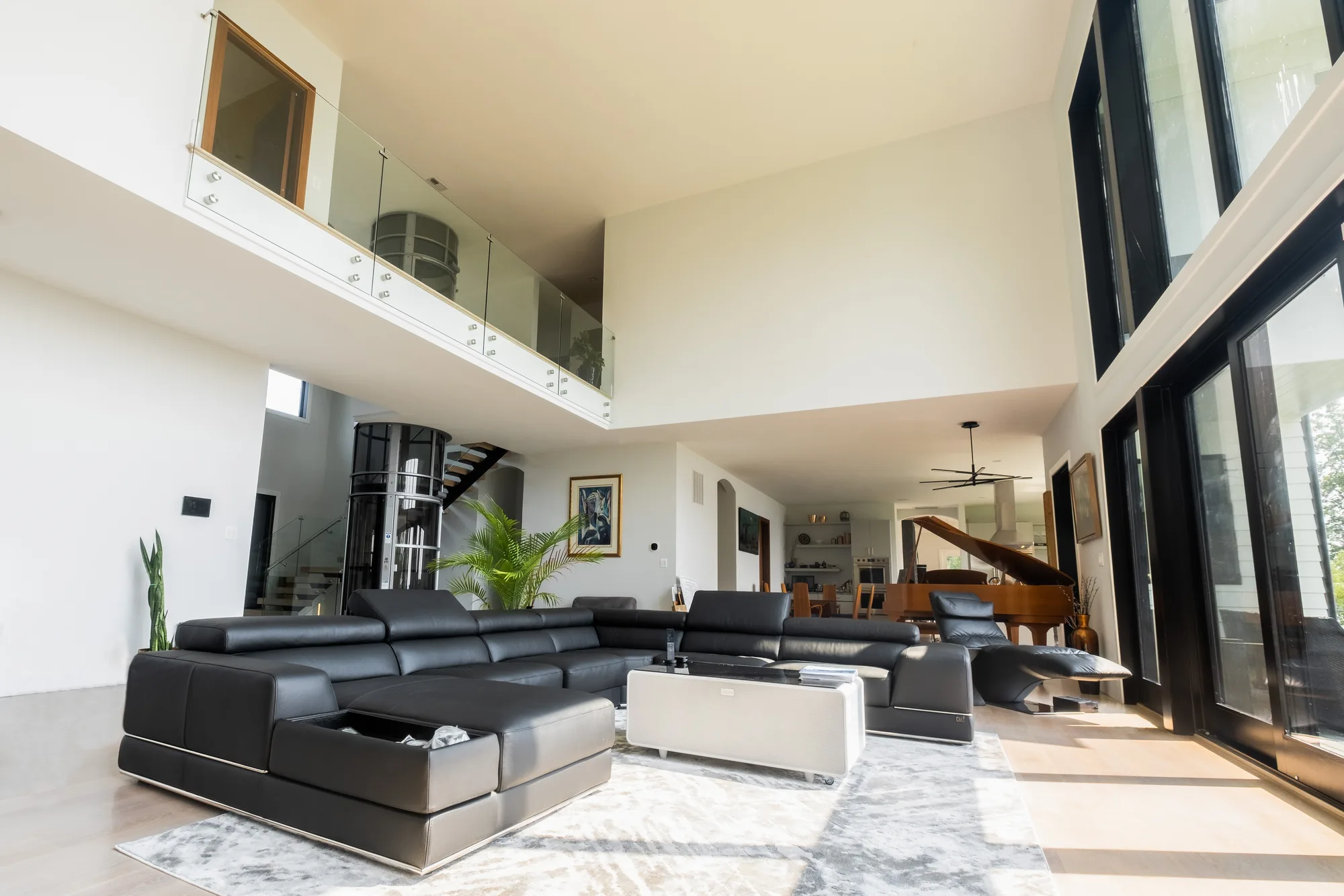 Double-height modern living room with leather sectional and glass railing loft in custom fabricated home, by OpenDoors360