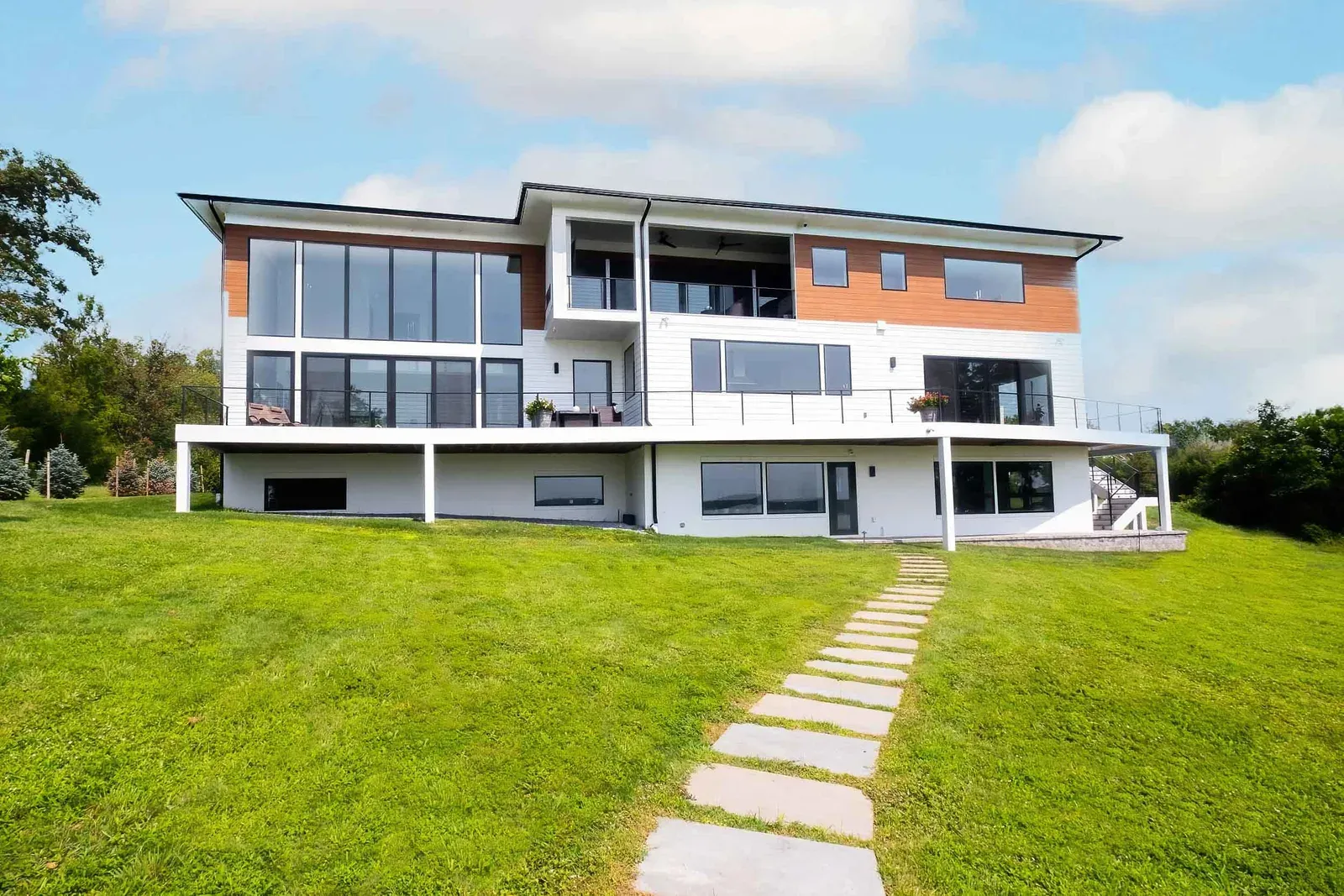 Contemporary multi-level home exterior with metal railings and stone pathway across green lawn, custom fabrication, by OpenDoors360