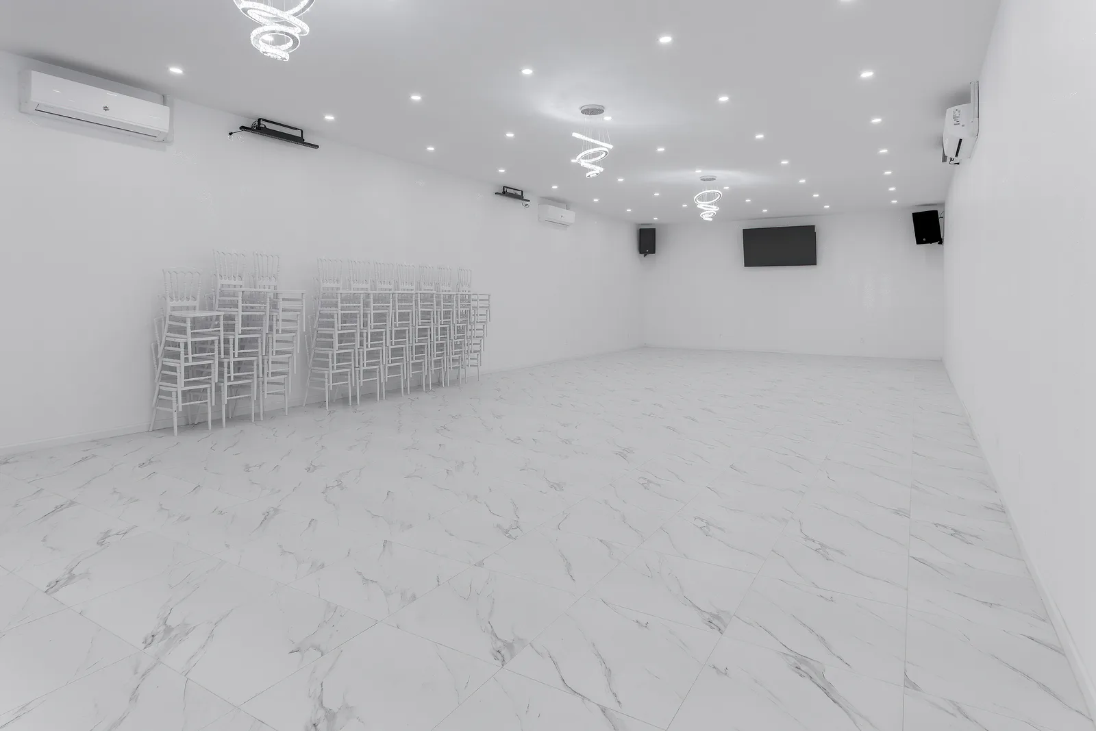 Bright white event hall with marble floors, ring chandeliers and stacked chiavari chairs at PartyRockers venue, by OpenDoors360