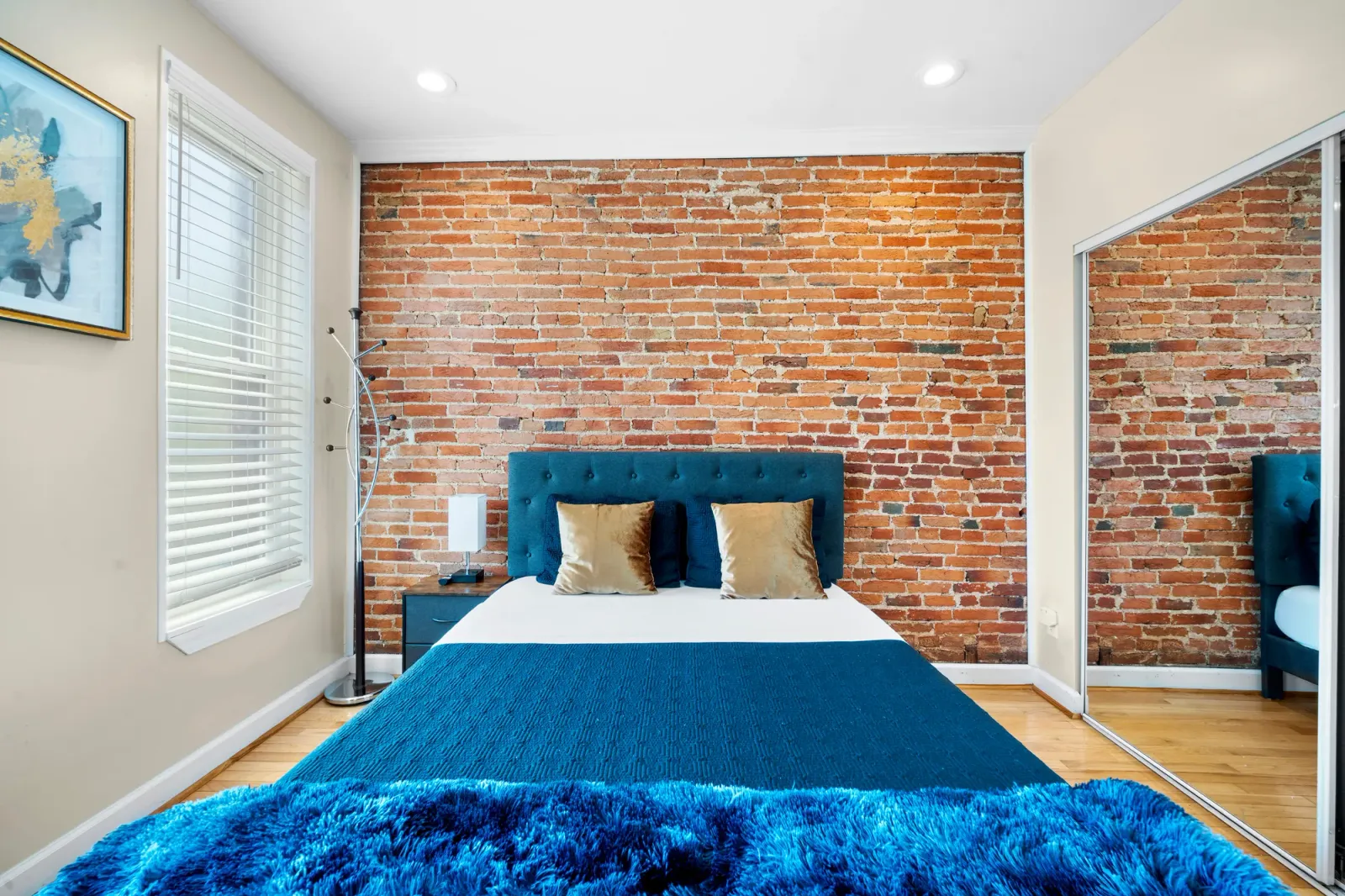 Bedroom with exposed brick wall and teal upholstered bed in Baltimore, MD, by OpenDoors360