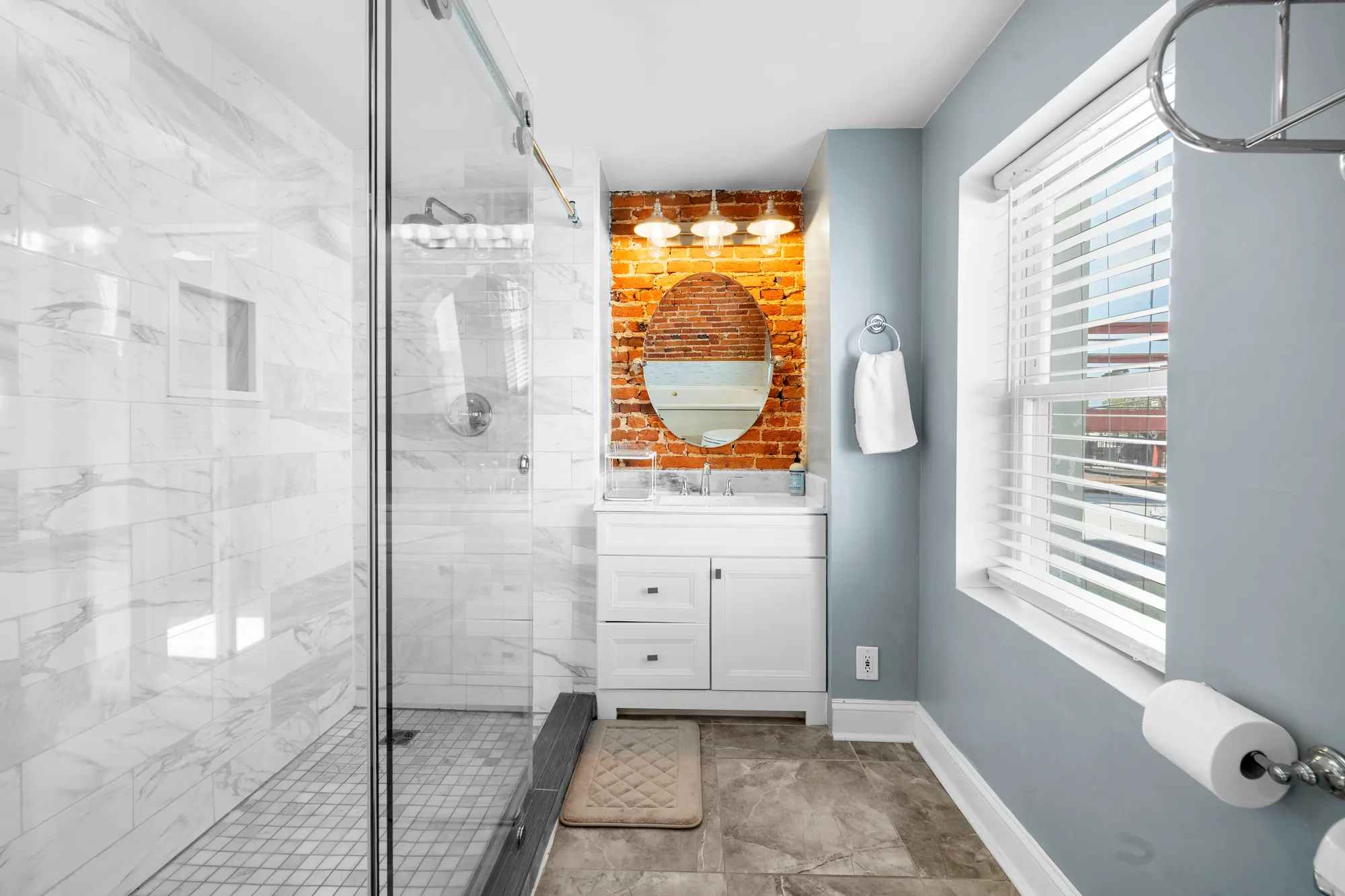 Bathroom with marble shower, brick niche and round mirror in Baltimore, MD, by OpenDoors360