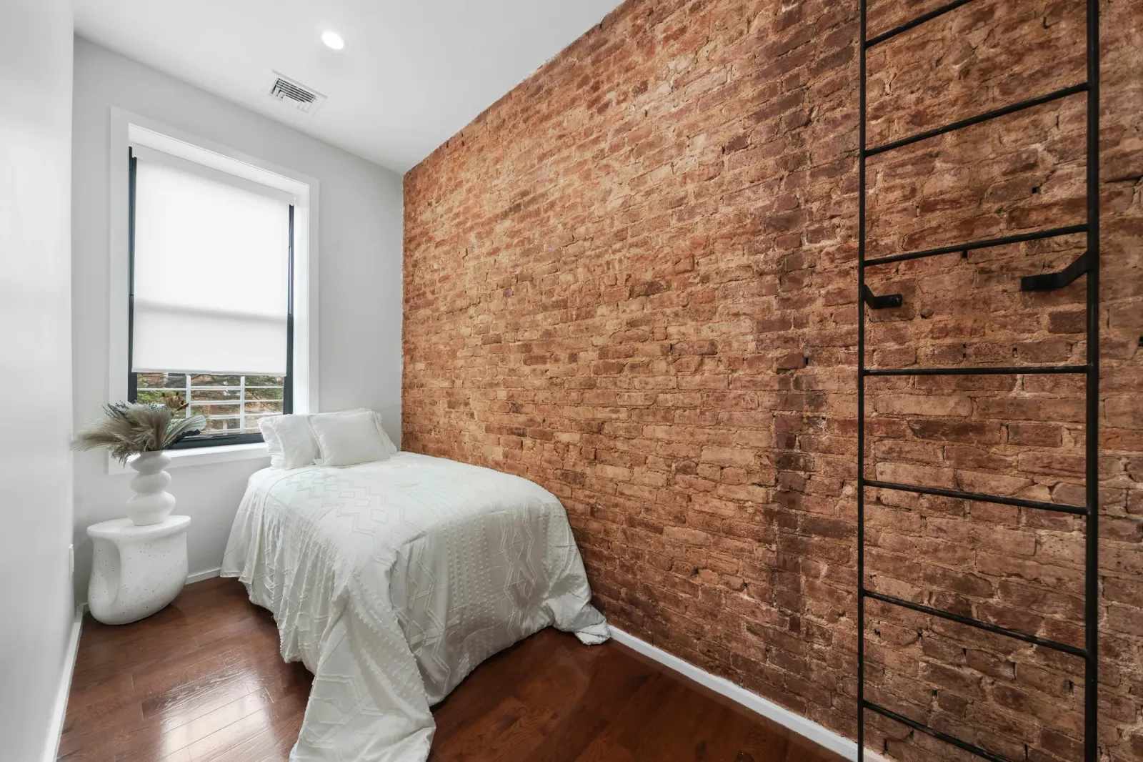 Small bedroom with full exposed brick wall and twin bed by sunny window, by OpenDoors360