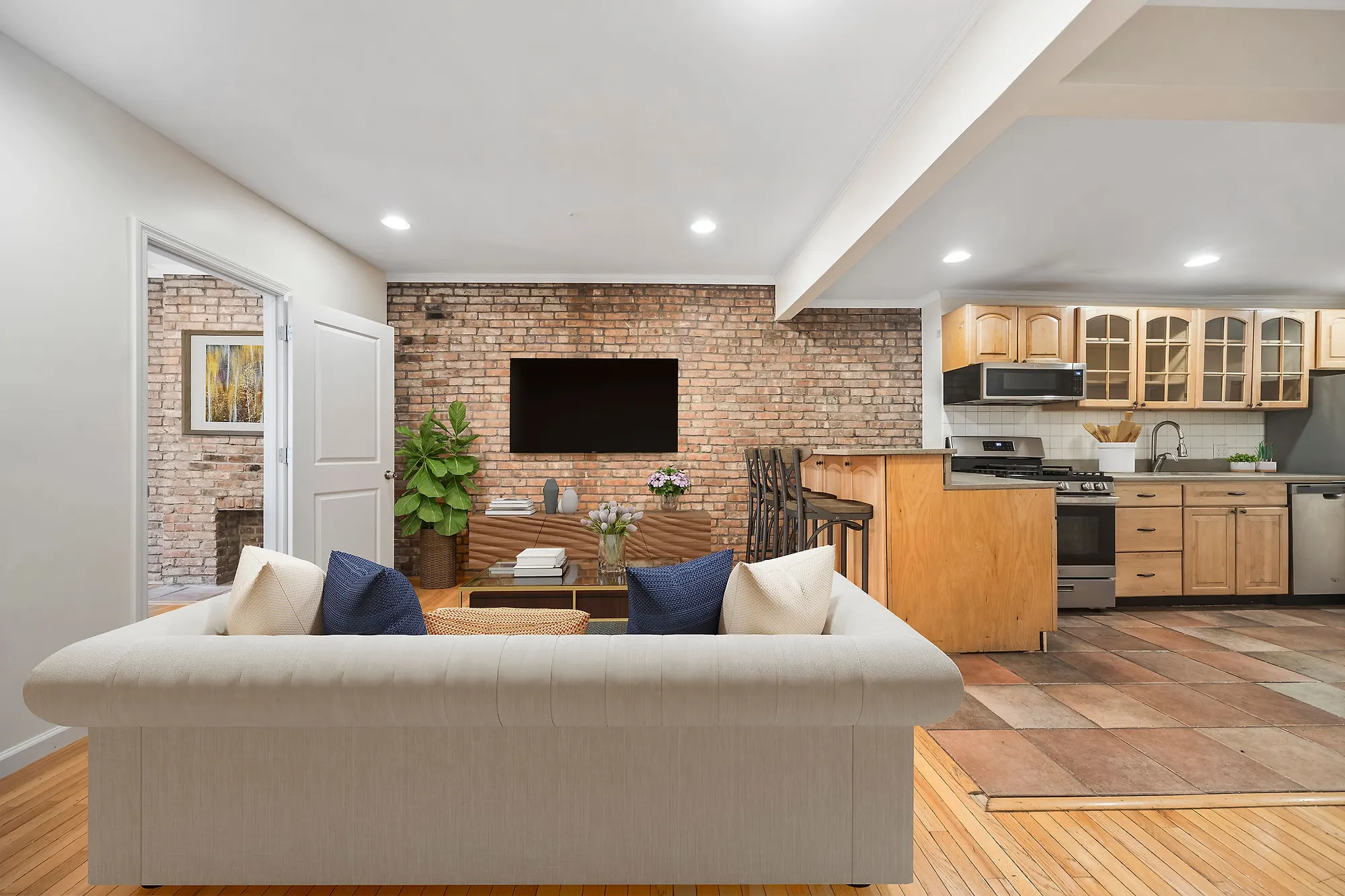 Virtually staged open living room and kitchen with exposed brick, a cream sofa and a wood breakfast bar, Upper East Side, by OpenDoors360