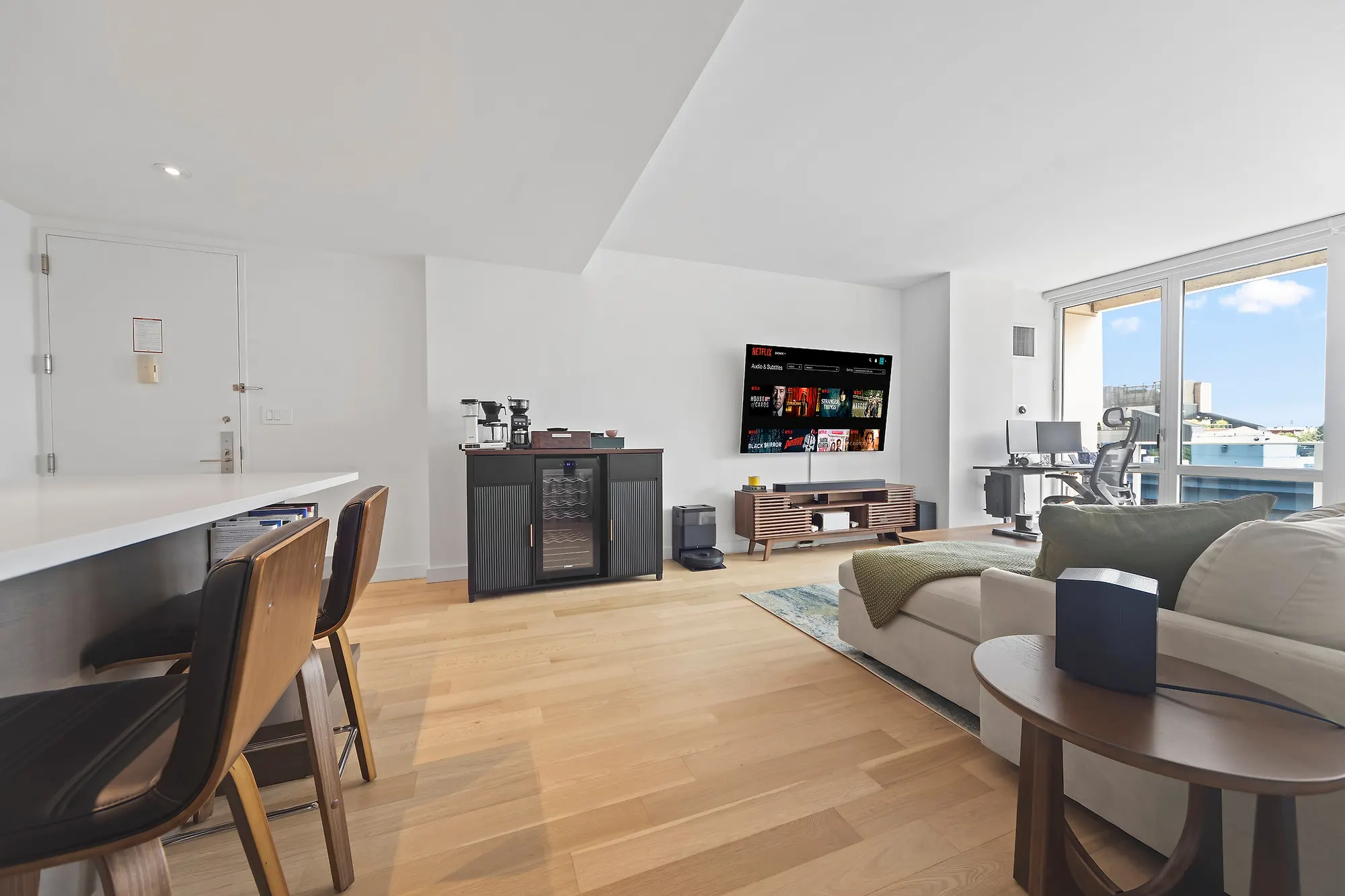 Living room in a Williamsburg condominium with a wall-mounted television, a sectional sofa and floor-to-ceiling glass to a balcony, by OpenDoors360