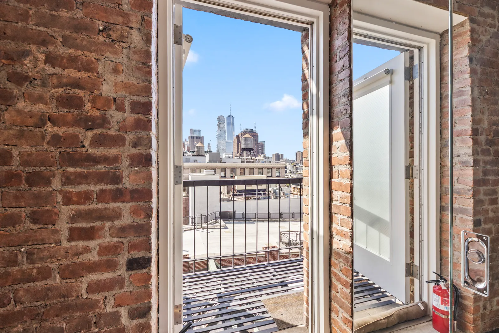 Open balcony doors in a brick wall framing One World Trade Center from a SoHo loft, by OpenDoors360