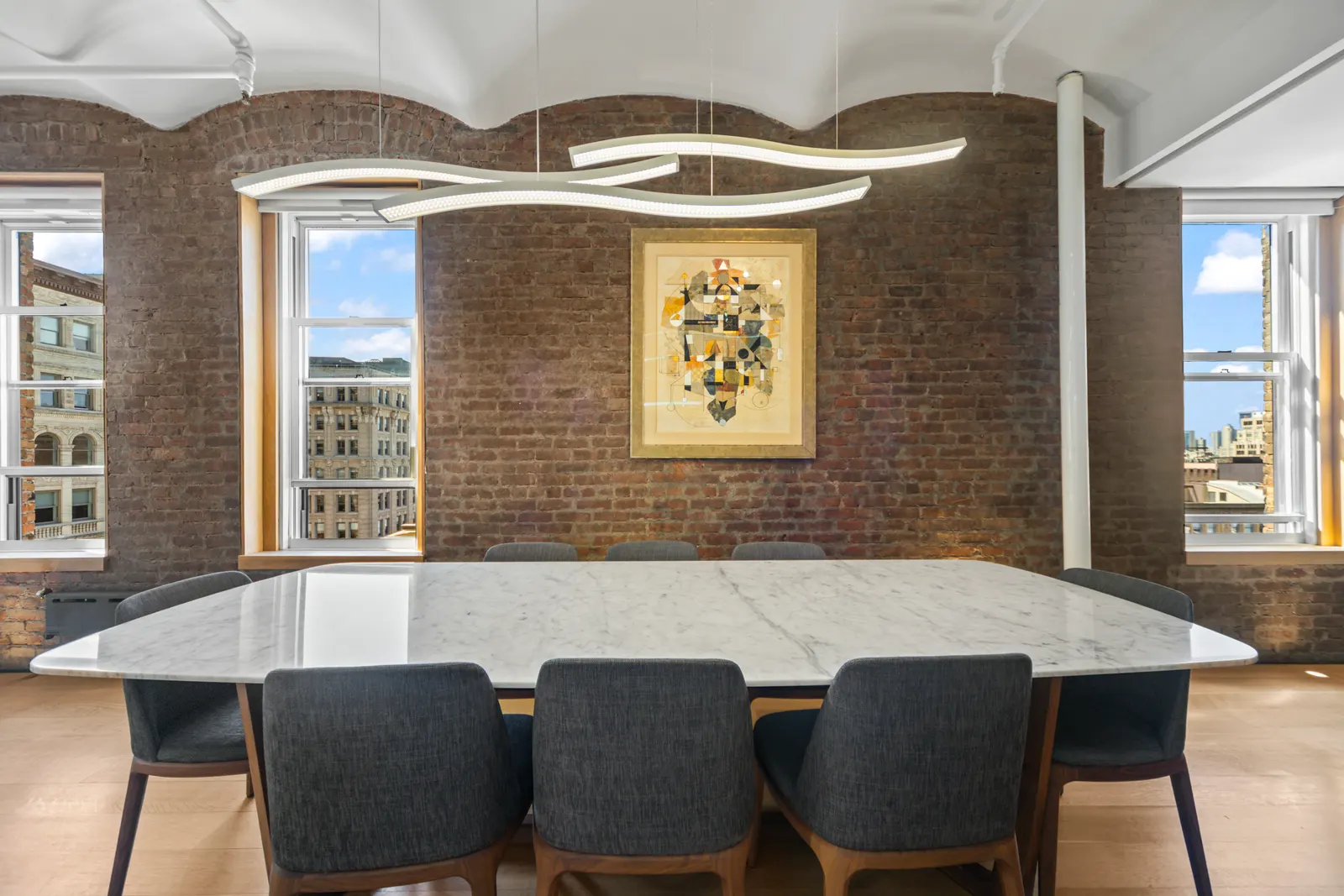 Marble dining table under a sculptural pendant between two brick-framed windows in SoHo, by OpenDoors360