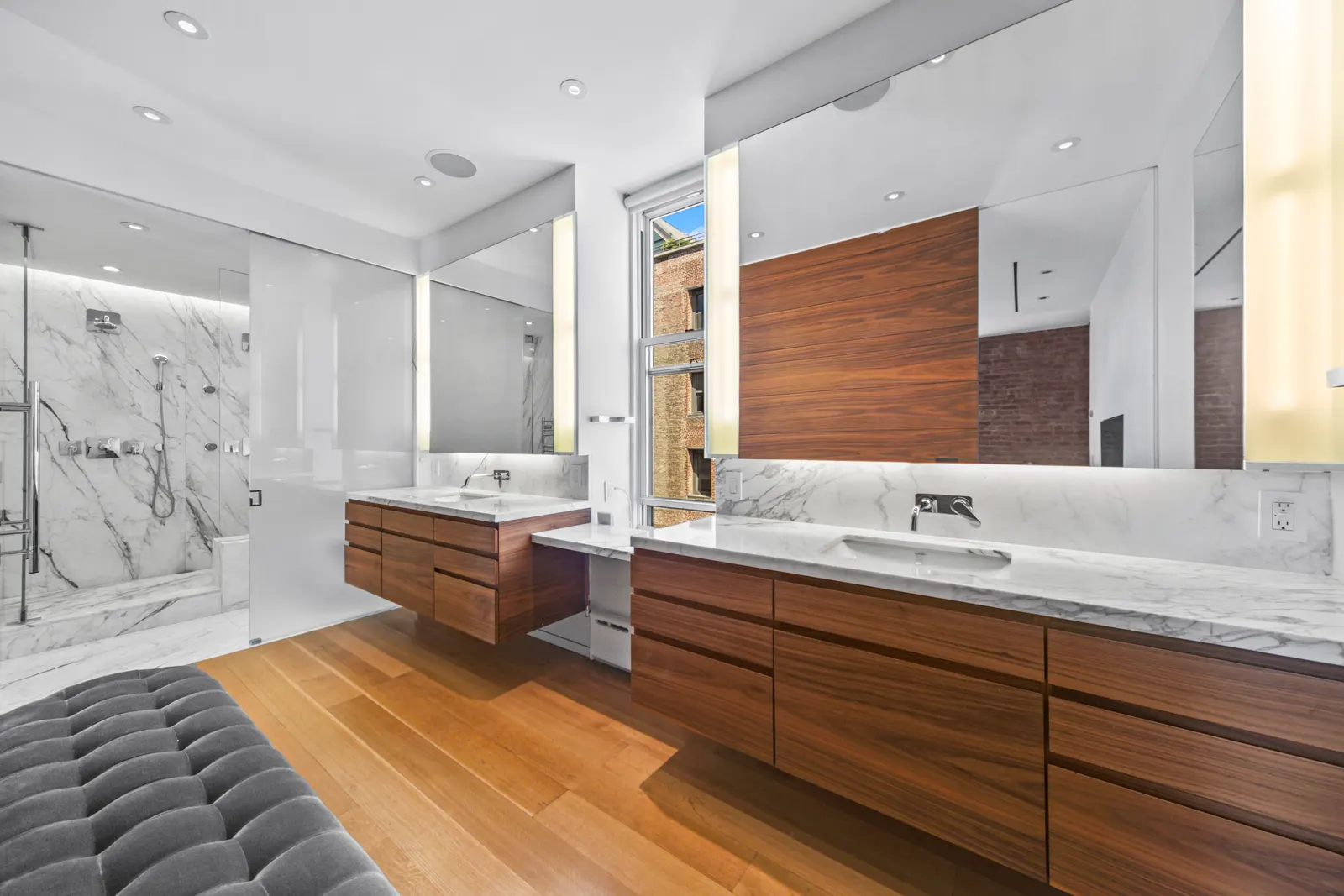 Walnut double vanity with marble counters and lit mirrors in a SoHo loft bathroom, by OpenDoors360