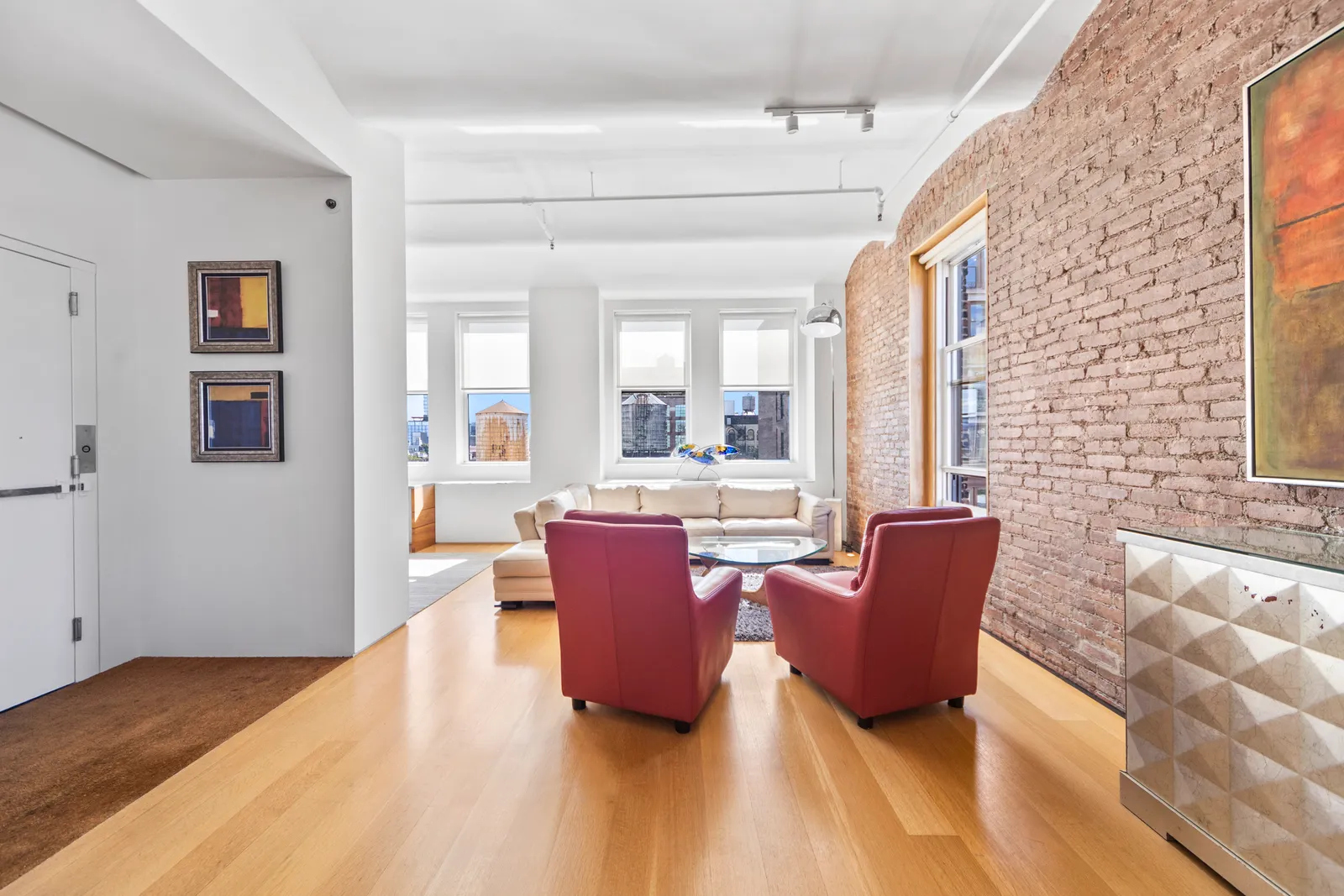 Entry hall opening onto the living room of a SoHo loft at 543 Broadway, with red leather armchairs and a row of windows, by OpenDoors360