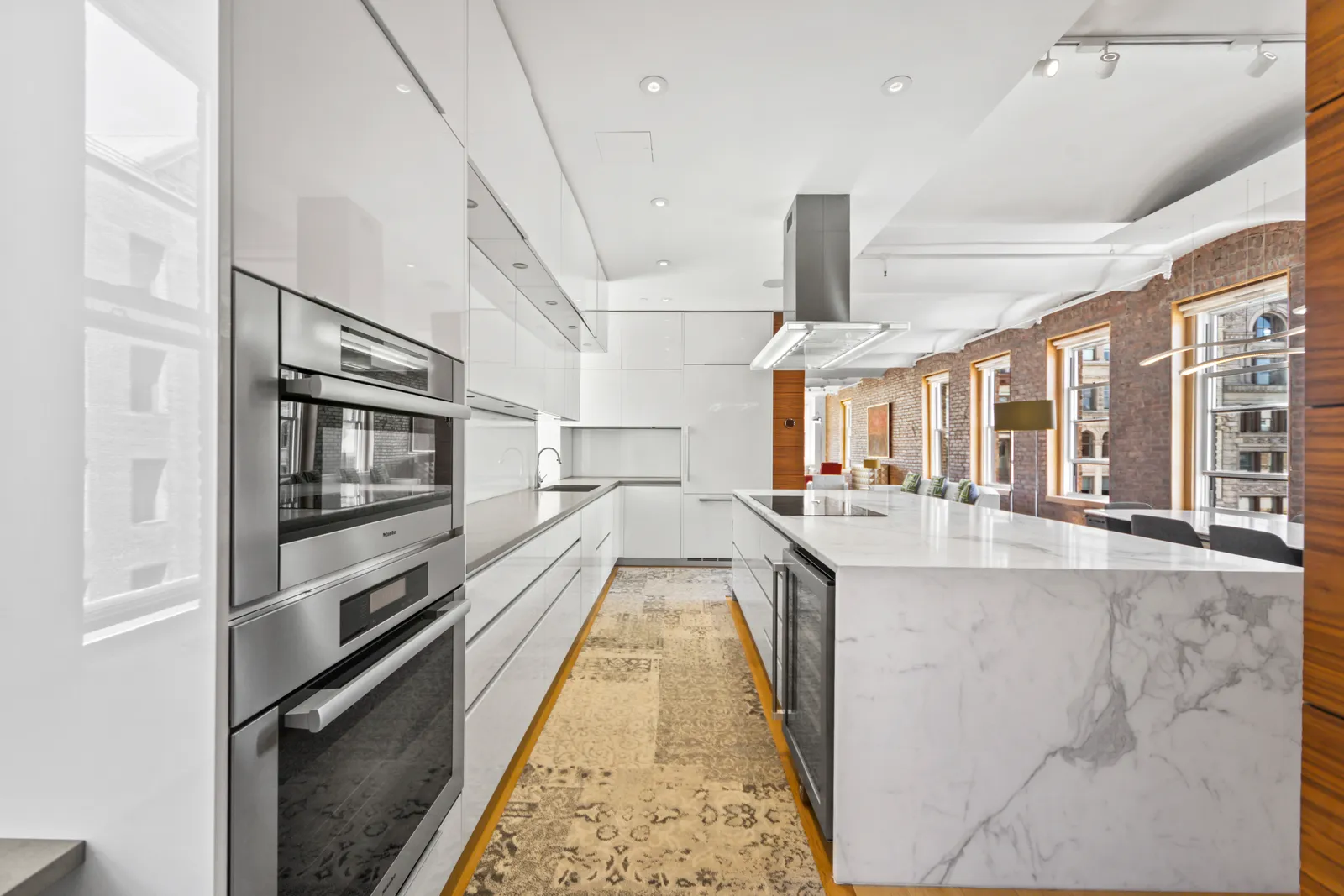 Stainless wall ovens along a white galley kitchen with a marble waterfall island in a SoHo loft, by OpenDoors360