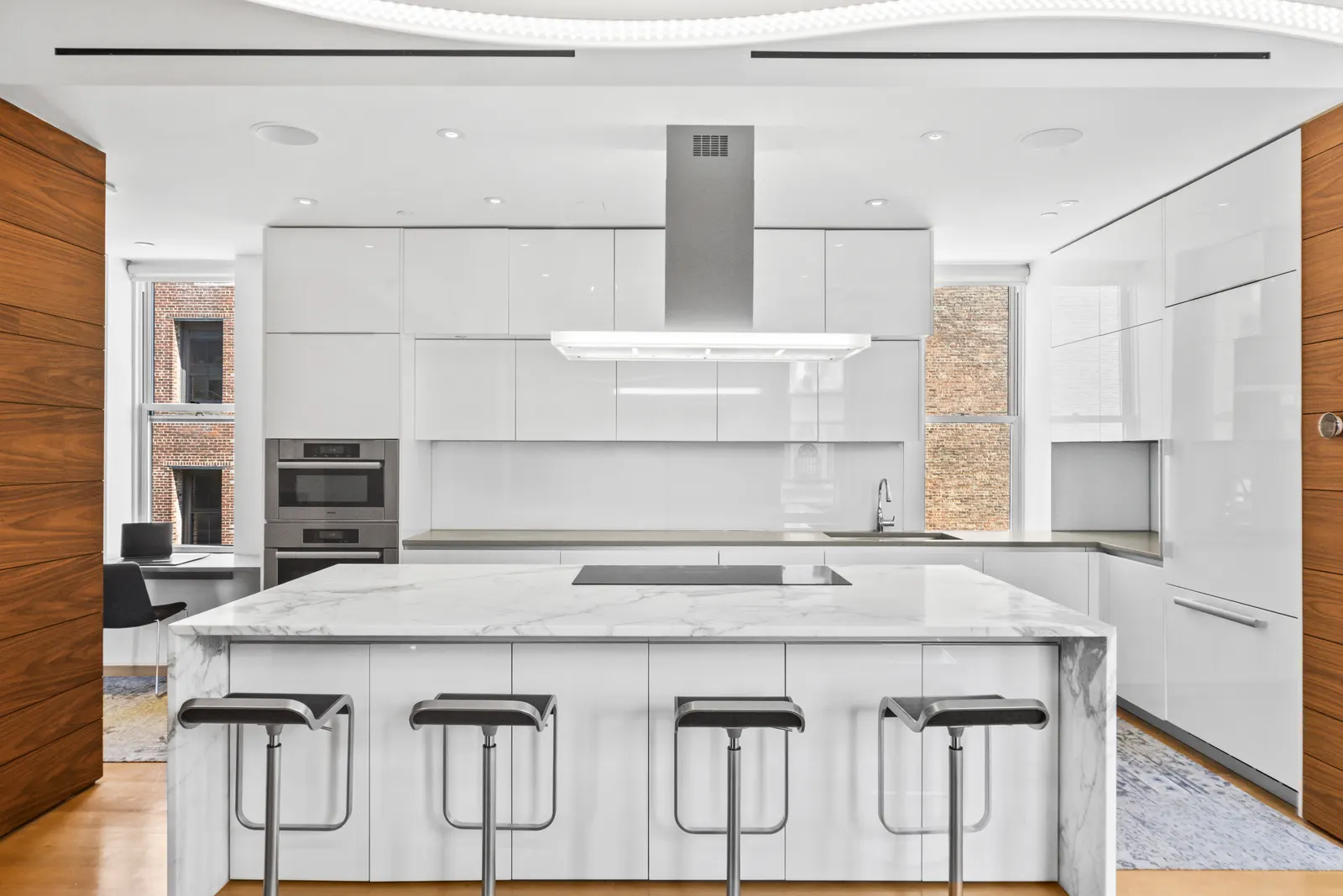 White lacquer kitchen with a marble island, bar stools and stainless wall ovens in a SoHo loft, Manhattan real estate photography by OpenDoors360