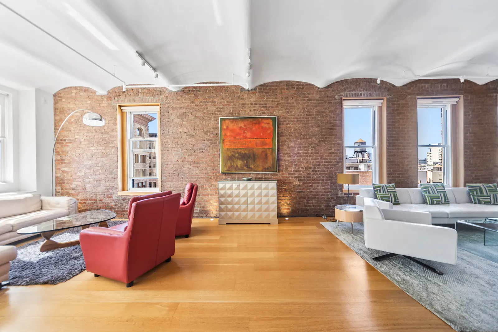 Living room of a SoHo loft with exposed brick, red leather armchairs, a cream sectional and tall windows, Manhattan real estate photography by OpenDoors360
