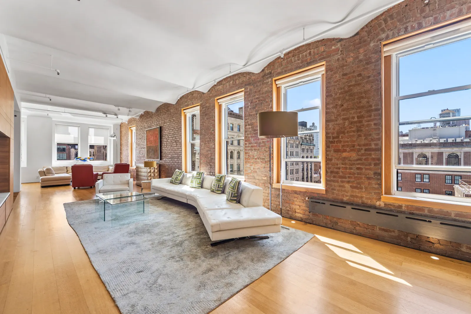 Long loft living room with brick window bays and a white sectional in SoHo, Manhattan, by OpenDoors360
