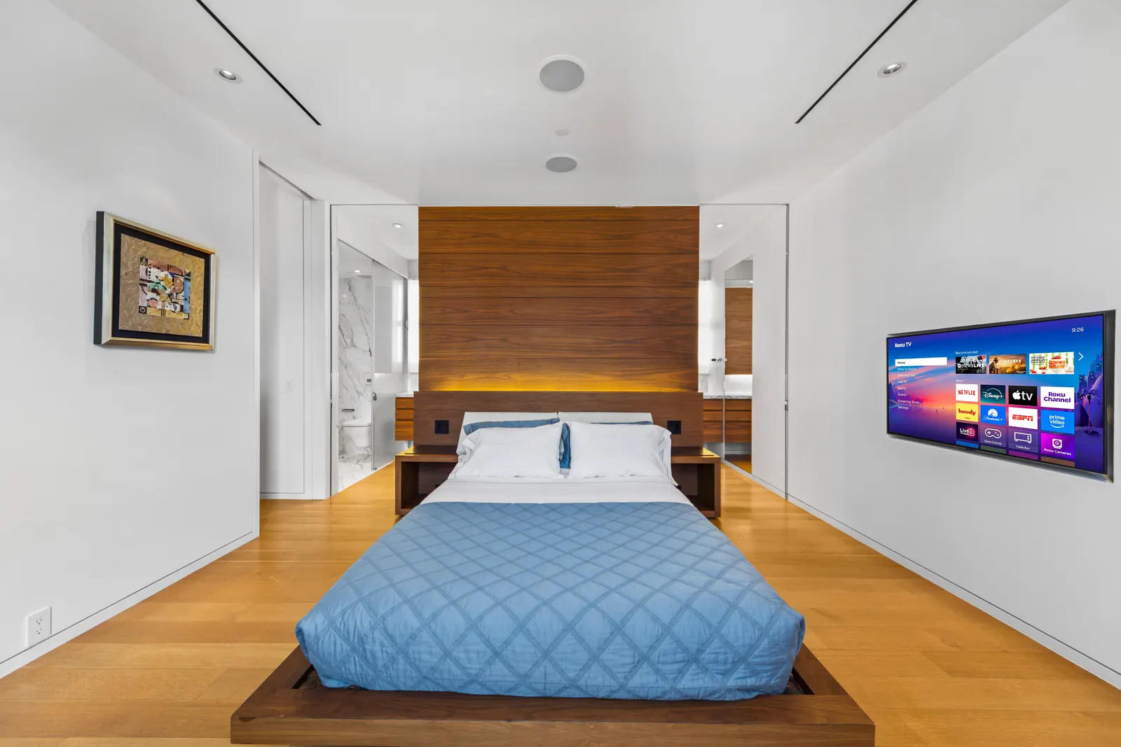 Primary bedroom with a walnut headboard wall and a blue quilt in a SoHo loft, by OpenDoors360