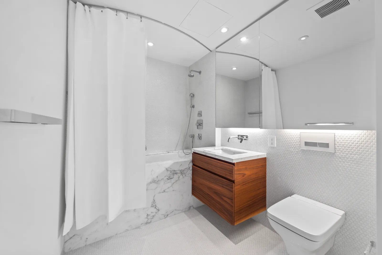 Second bathroom with a floating walnut vanity, marble tub surround and wall-hung toilet in a SoHo loft, by OpenDoors360