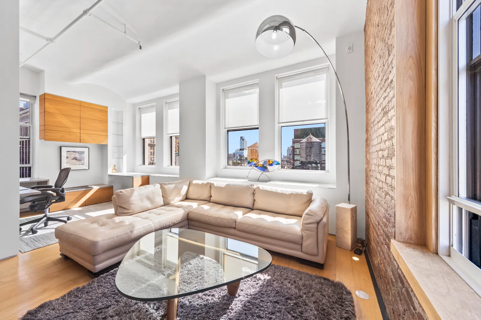 Cream leather sectional, glass coffee table and arc floor lamp by tall windows in a SoHo loft, photographed on the same shoot as its video walkthrough by OpenDoors360
