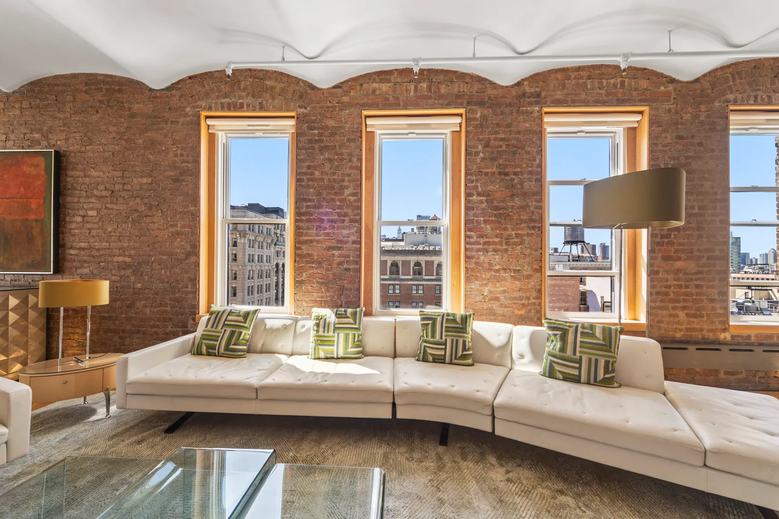 Curved white leather sofa under a row of brick-framed windows in a Manhattan loft, by OpenDoors360