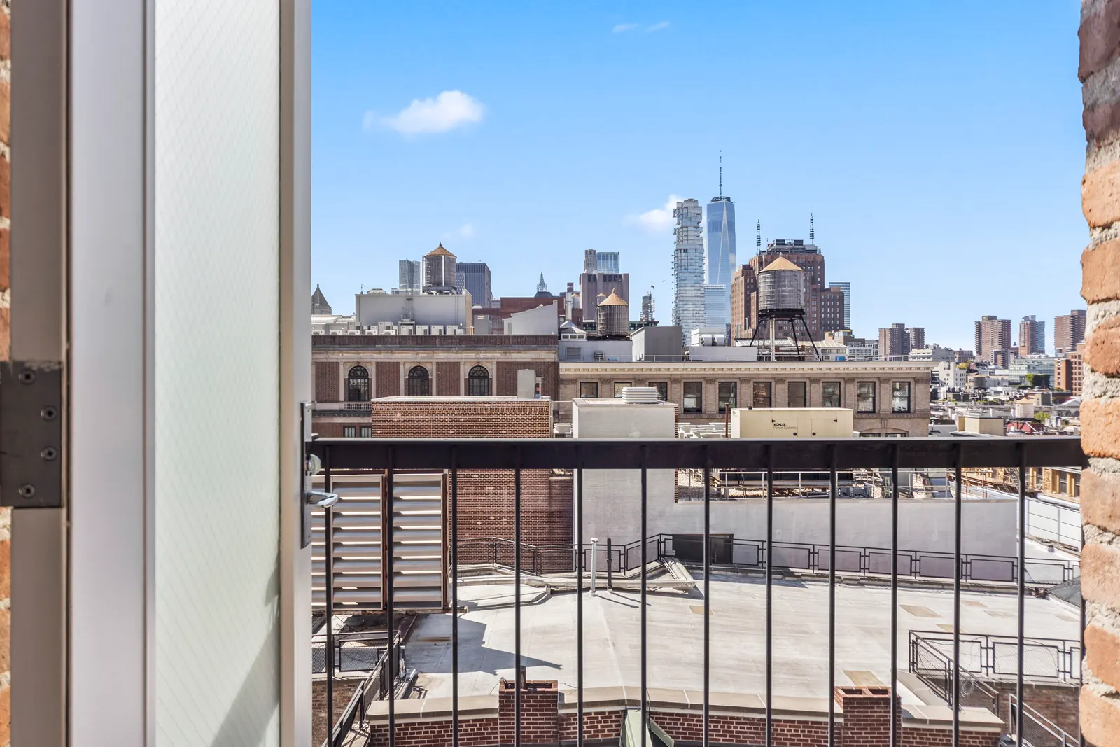 Open loft window with an iron balcony rail looking over SoHo rooftops to One World Trade Center, Manhattan real estate photography by OpenDoors360