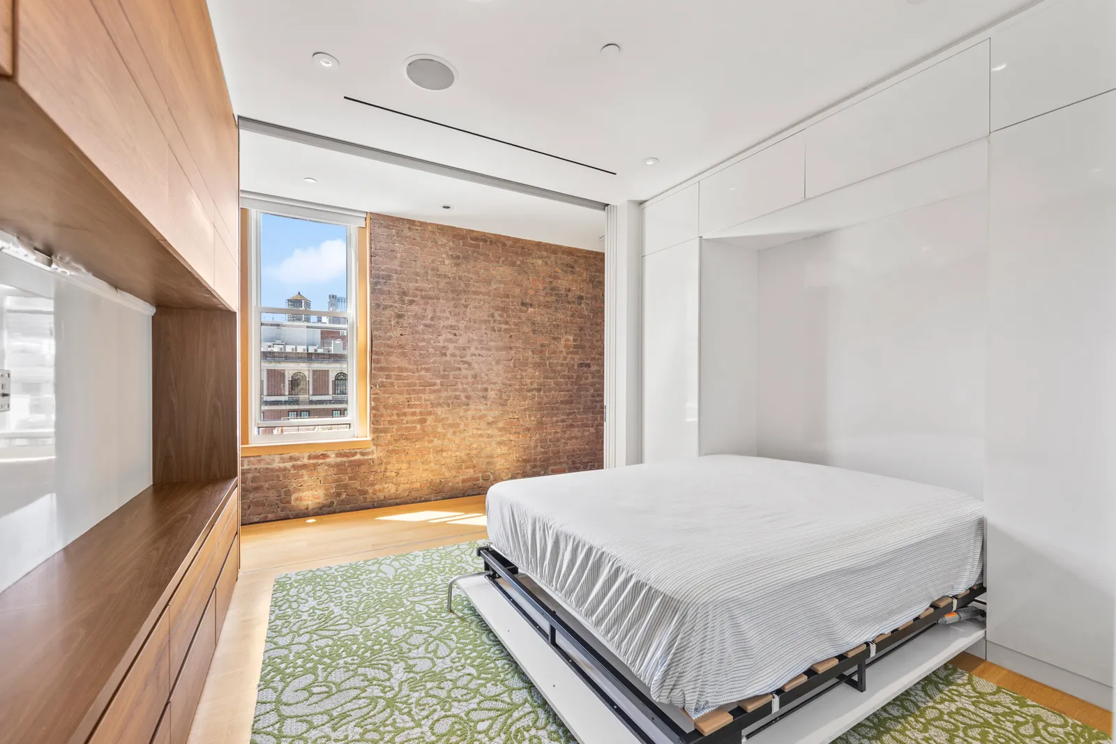 Room with a fold-down wall bed, a green patterned rug and exposed brick in a SoHo loft, by OpenDoors360