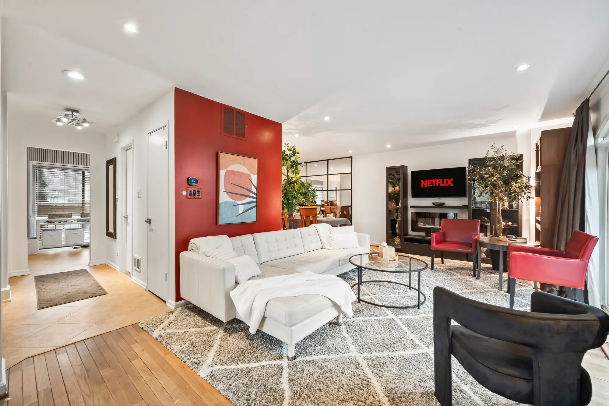 OpenDoors360 short term rental photography of an open living room with a red accent wall, sectional sofa, and hardwood floors, shot from a corner to show depth without distortion