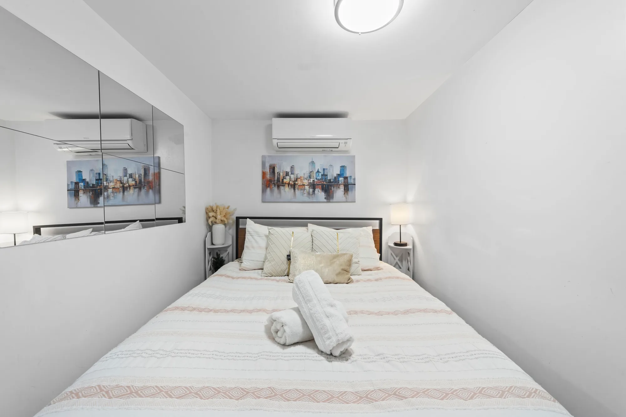 Compact bedroom with mirrored wall, mini-split AC and city skyline art, by OpenDoors360