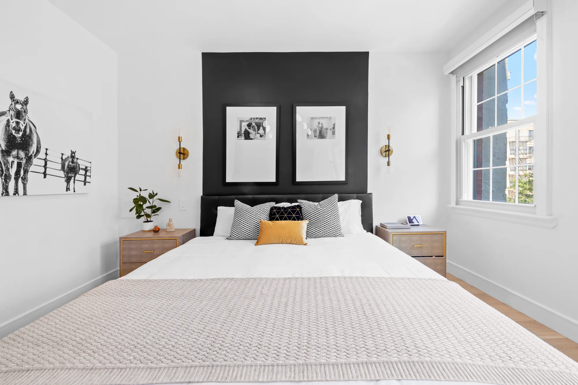 Bright bedroom with black accent wall, framed prints, brass sconces, and yellow accent pillow, by OpenDoors360