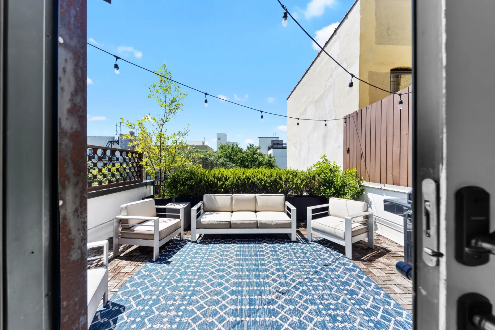 Private rooftop terrace with white wicker sofa, string lights, and blue patterned outdoor rug, by OpenDoors360