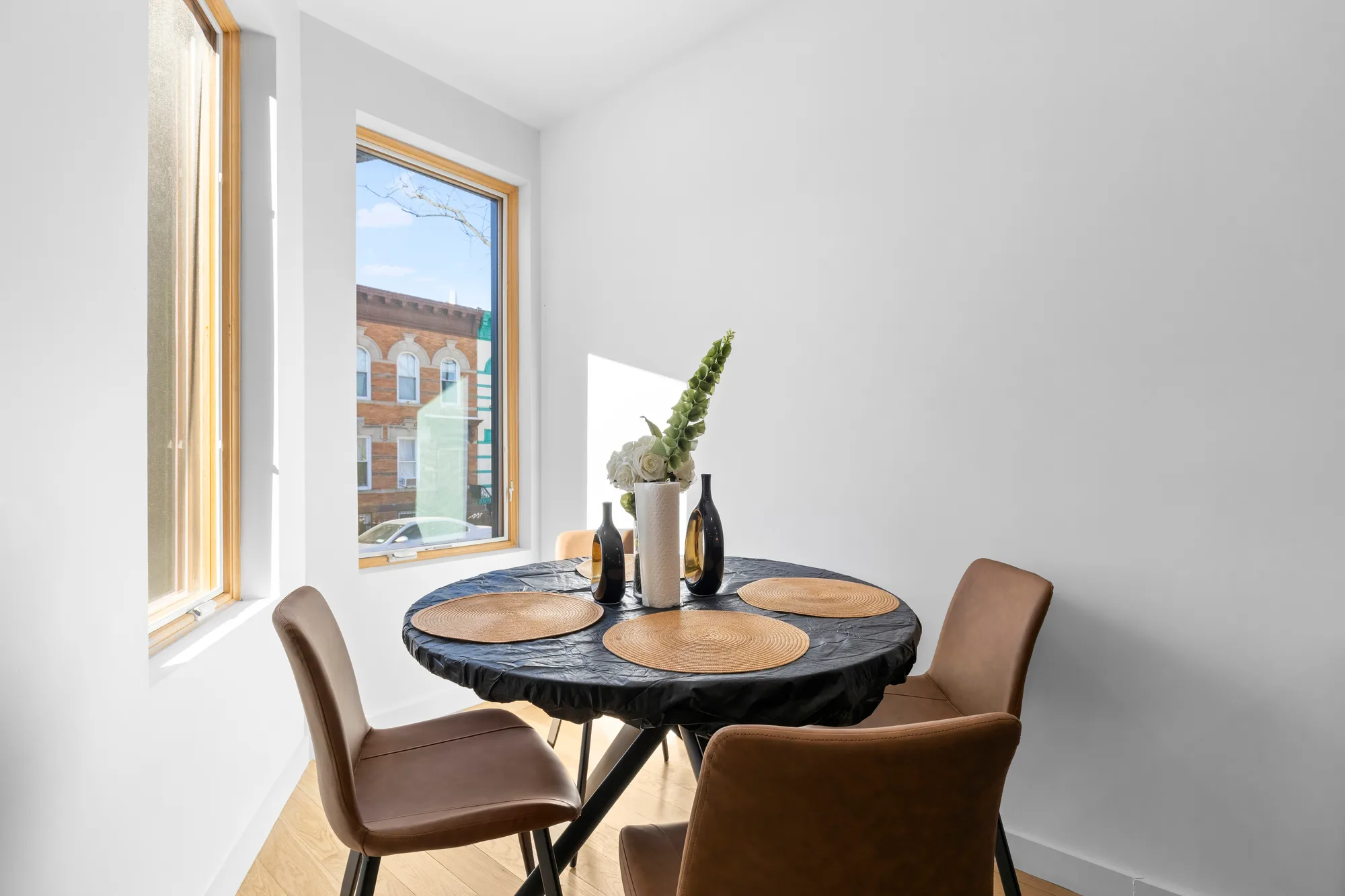 Sunlit breakfast nook with round table, leather chairs, and window over Brooklyn rowhouses, by OpenDoors360