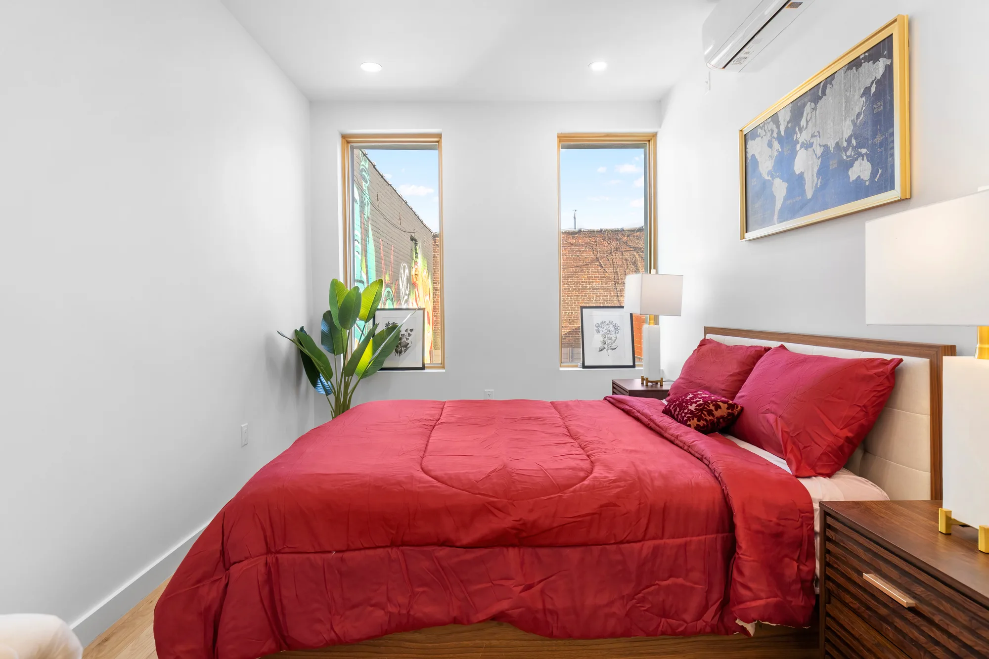 Hallway view between two staged bedrooms with round gold mirror and tall potted plant, by OpenDoors360