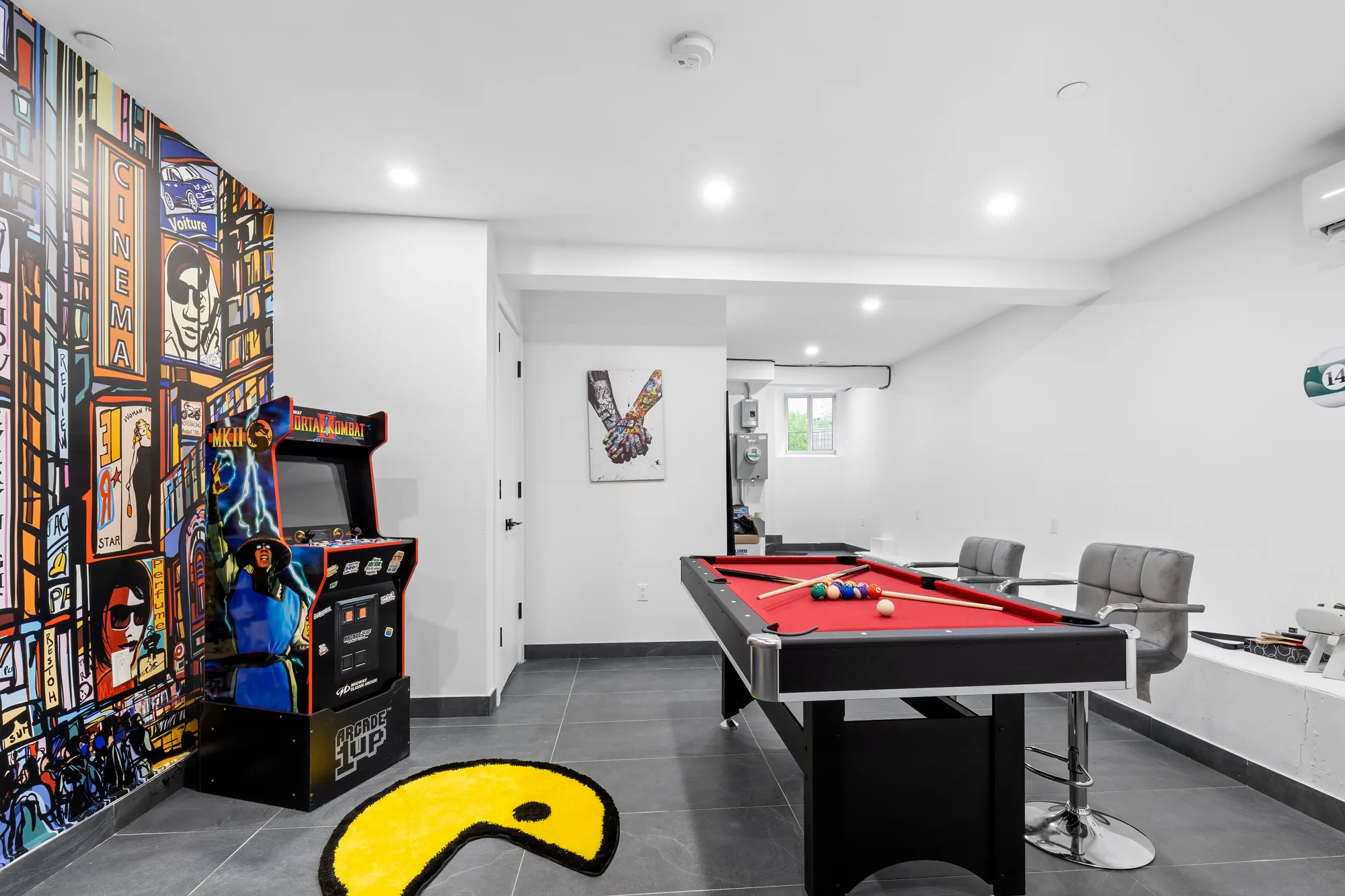 Basement games room with red pool table, arcade machines, and pop-art Times Square mural, by OpenDoors360