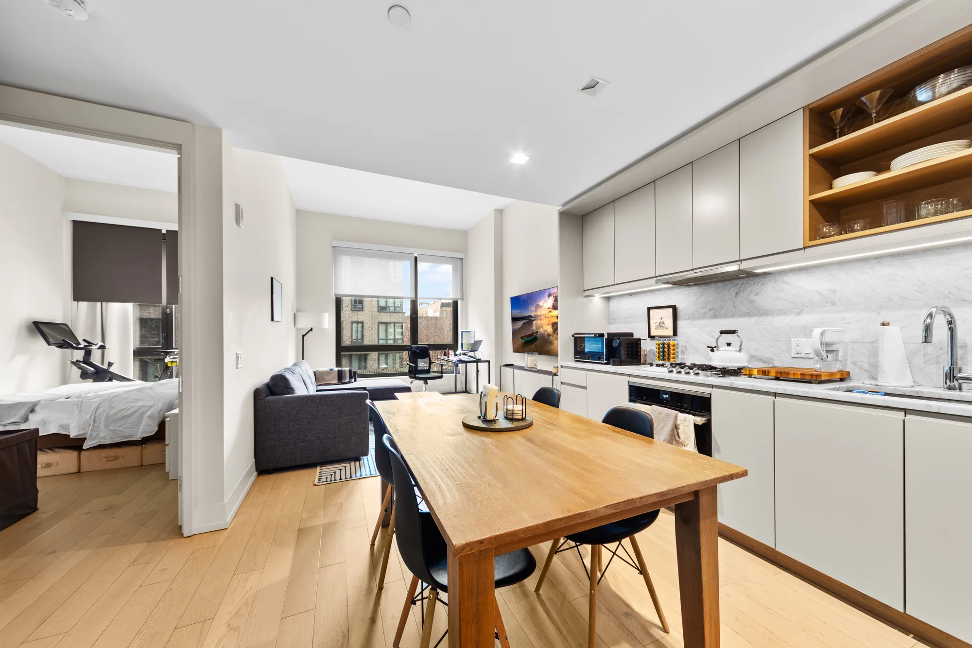 Open studio kitchen with gray cabinets, marble backsplash, dining table, and bedroom beyond, by OpenDoors360