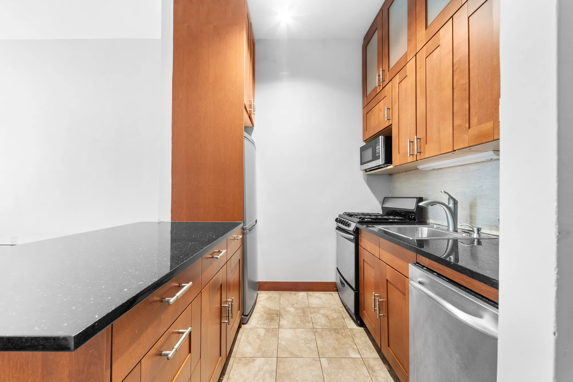 Galley kitchen with cherry wood cabinets, black speckled granite counters, and stainless appliances, by OpenDoors360