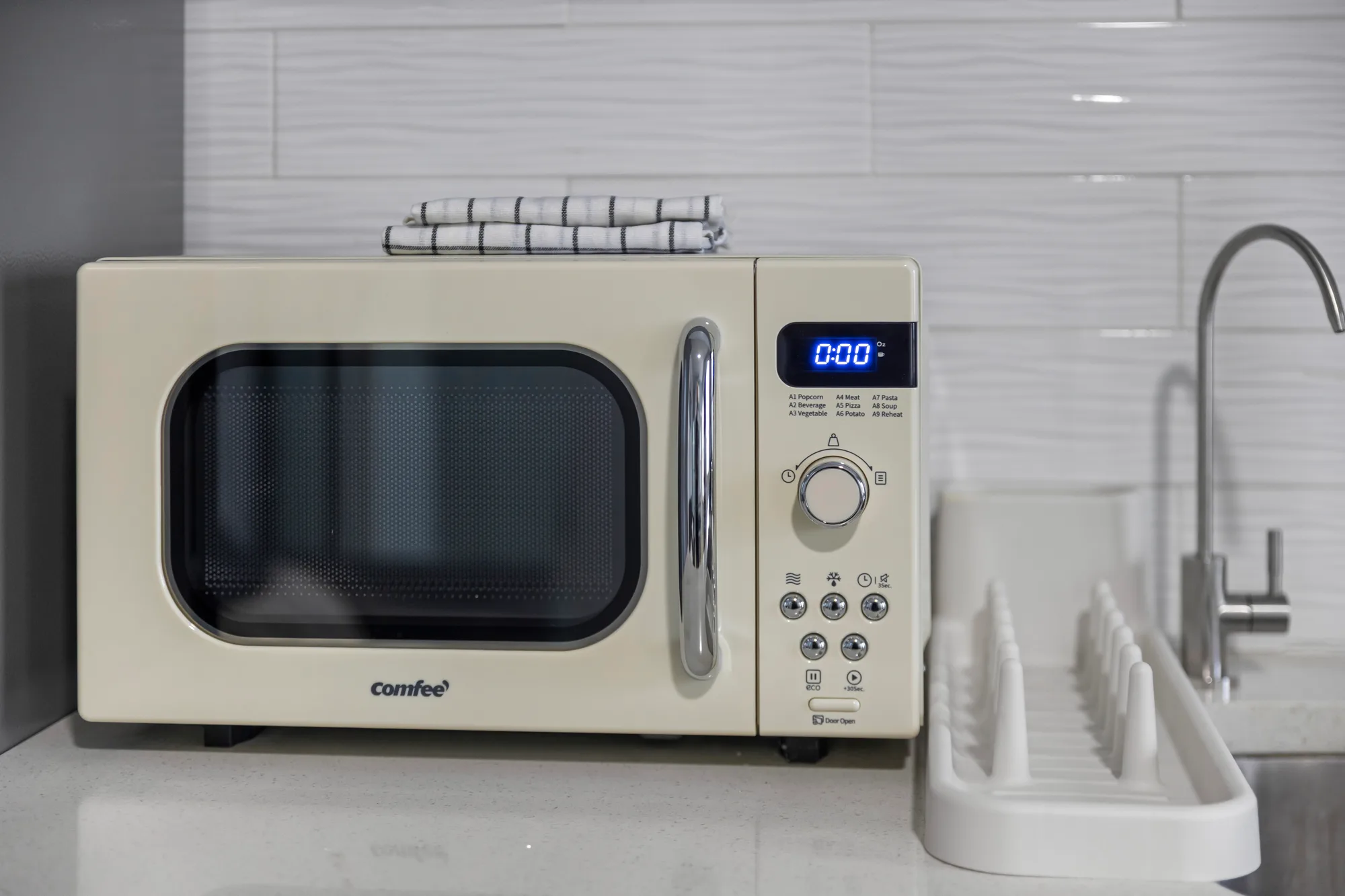 Cream retro Comfee microwave and white dish rack on a kitchen counter beside a filtered-water faucet, by OpenDoors360