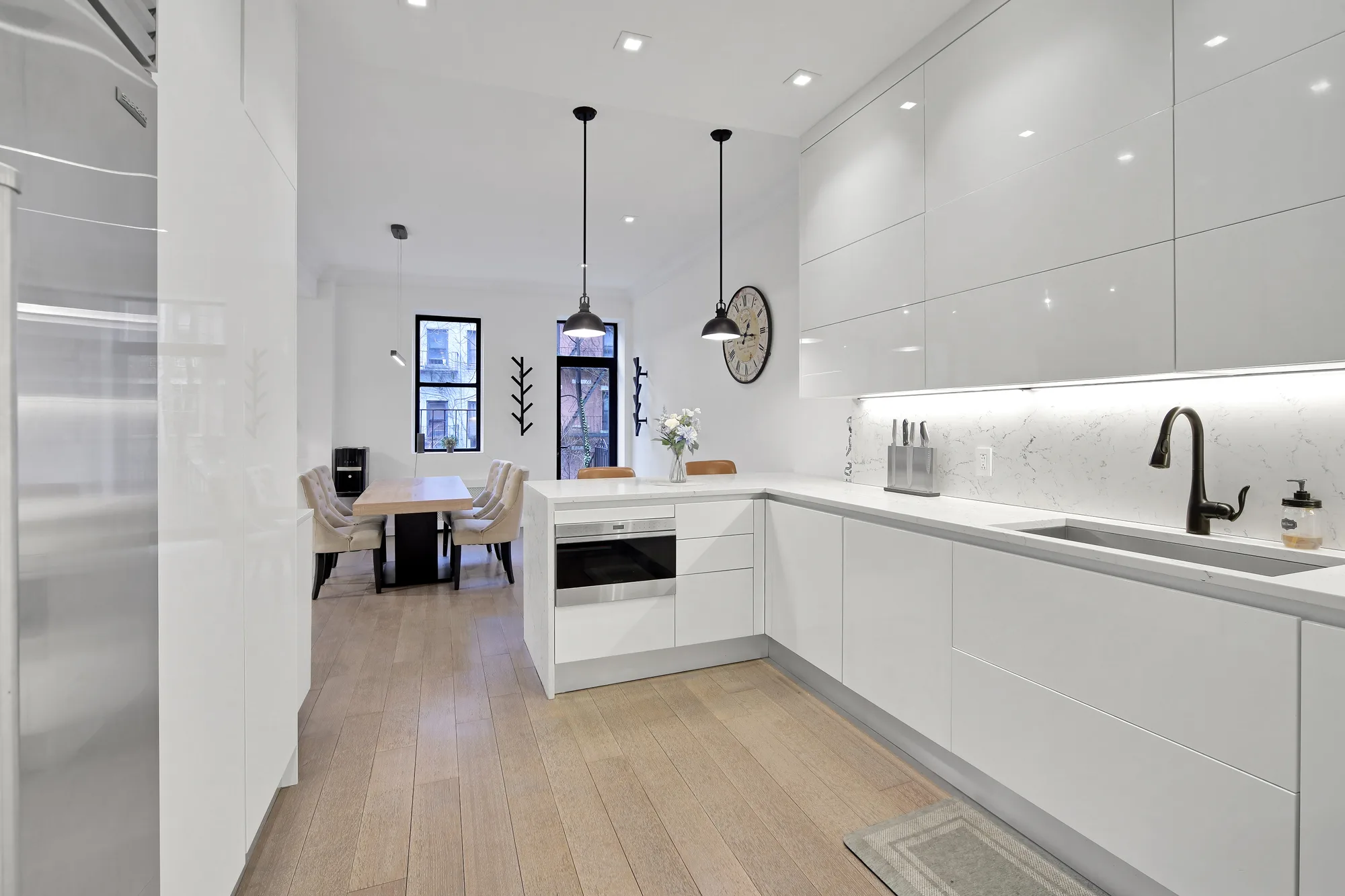 Modern white high-gloss kitchen with quartz counters, pendant lights, and open dining beyond, by OpenDoors360