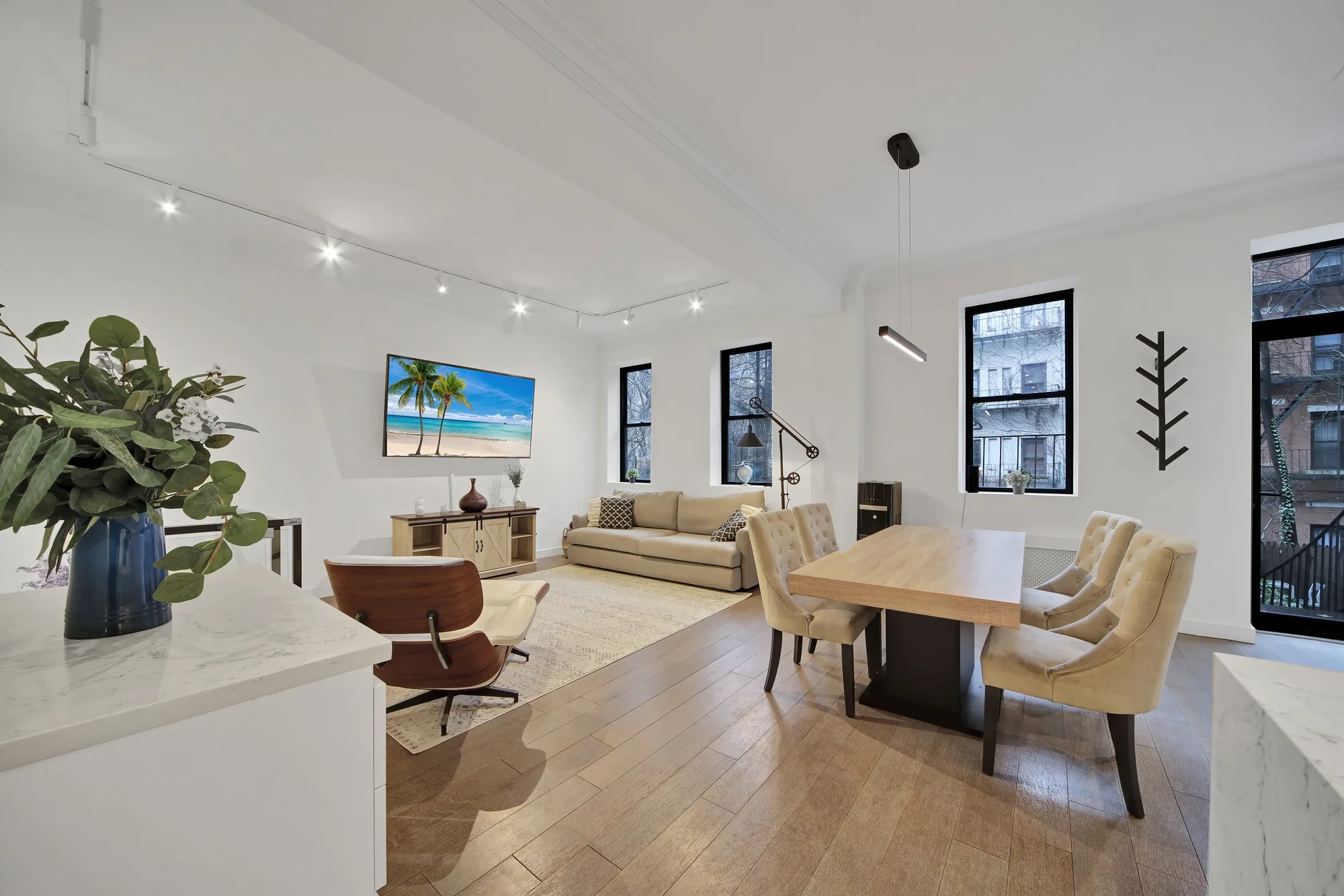 Open living and dining space with beamed ceiling, beige sofa, tufted chairs, and beach art on TV, by OpenDoors360