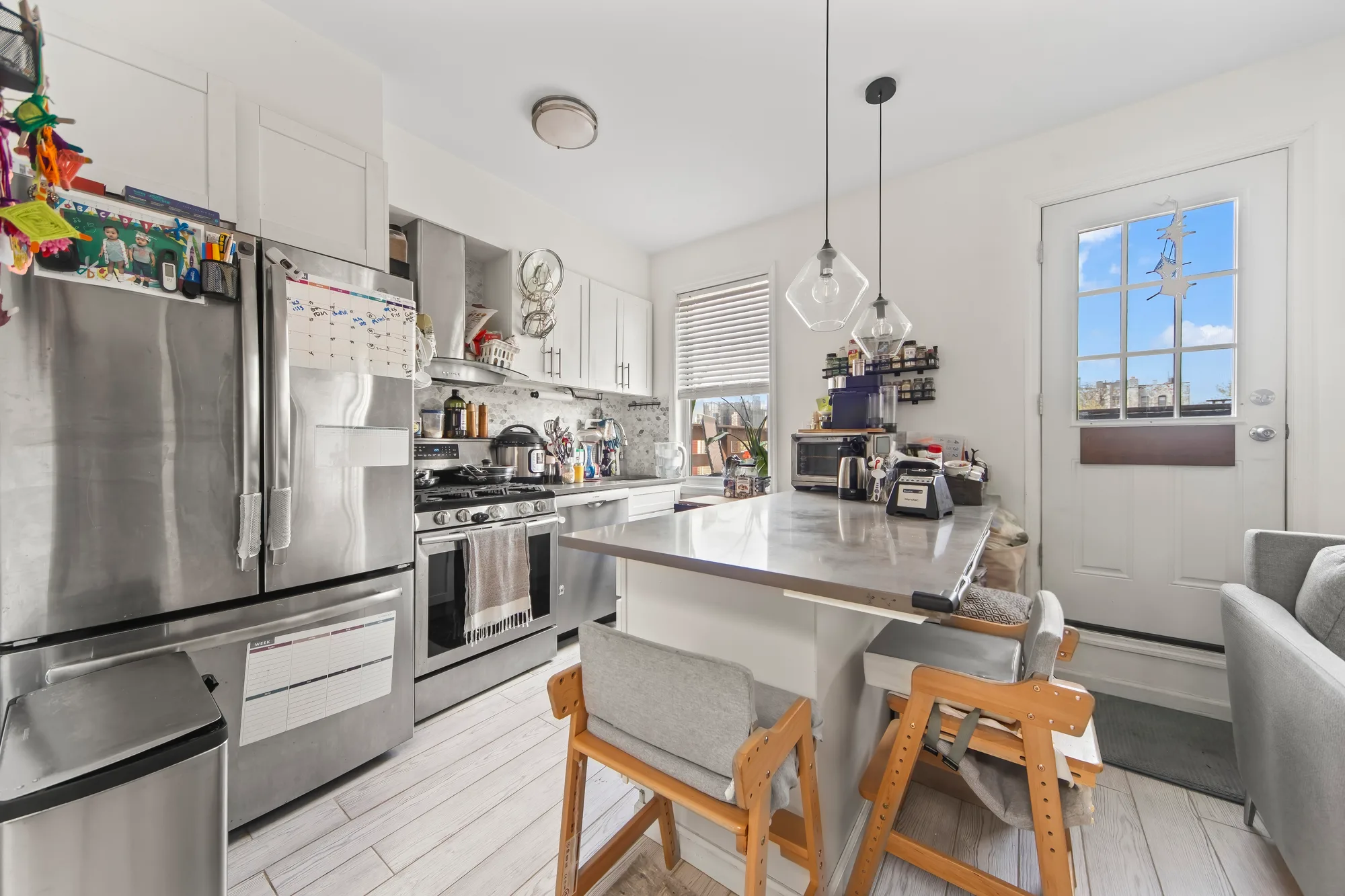 Lived-in kitchen with stainless steel island, glass pendant lights, and glass-paned back door, by OpenDoors360