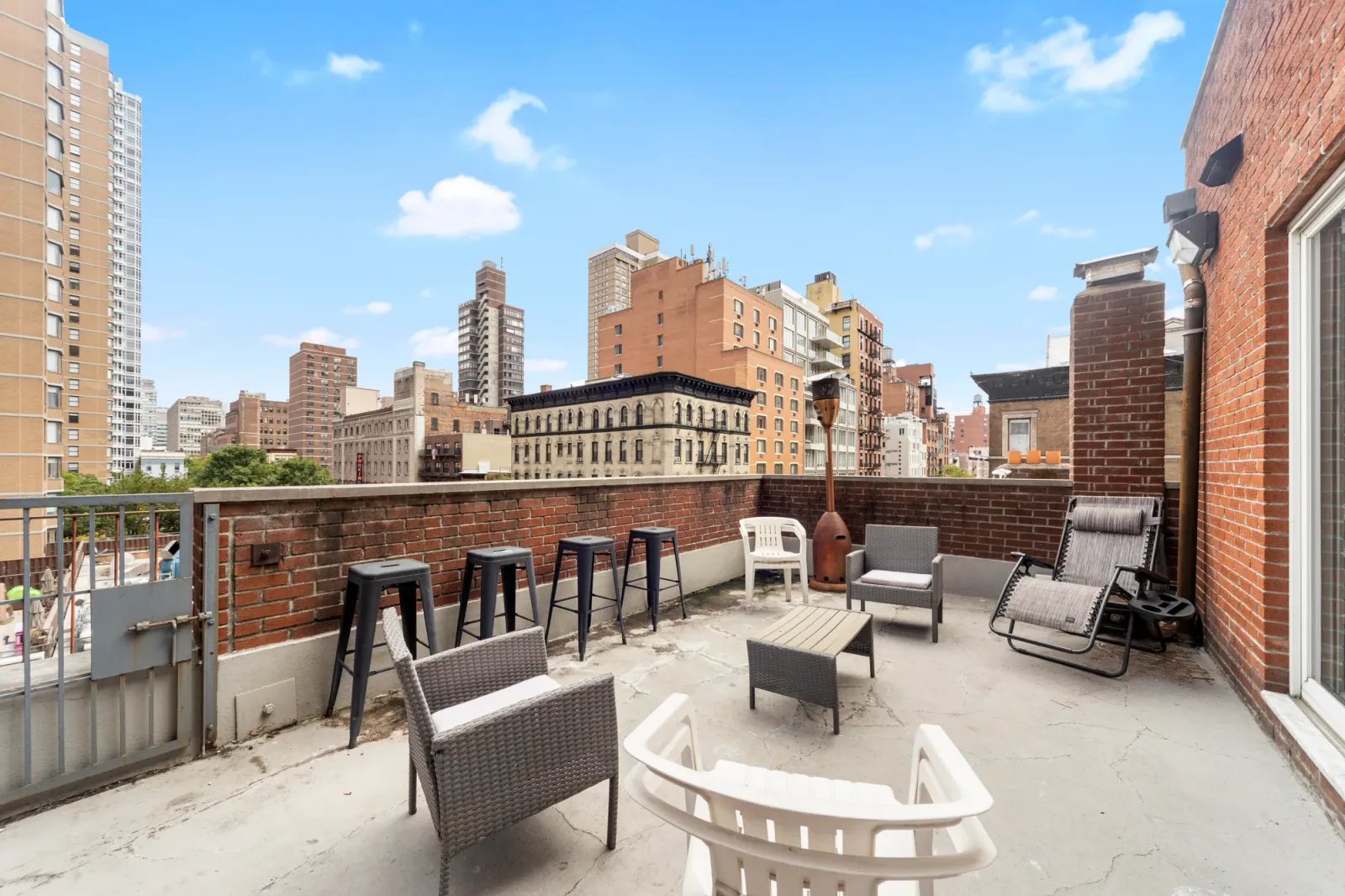 Private city rooftop terrace with bar stools, lounge chairs, and skyline of brick high-rises, by OpenDoors360