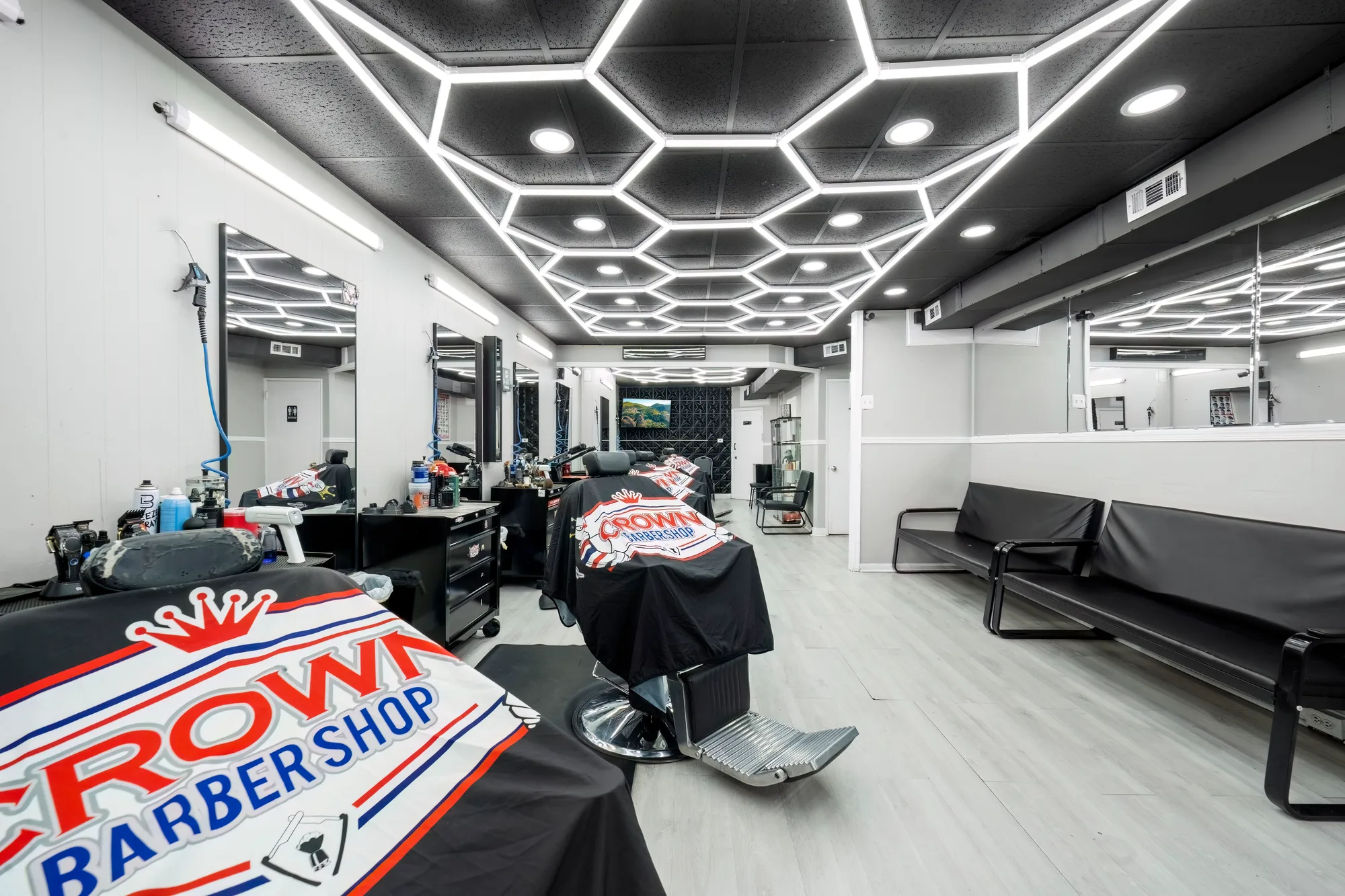 Crown Barbershop with branded chair cape, hexagon ceiling lights, mirrored stations, and waiting bench, by OpenDoors360