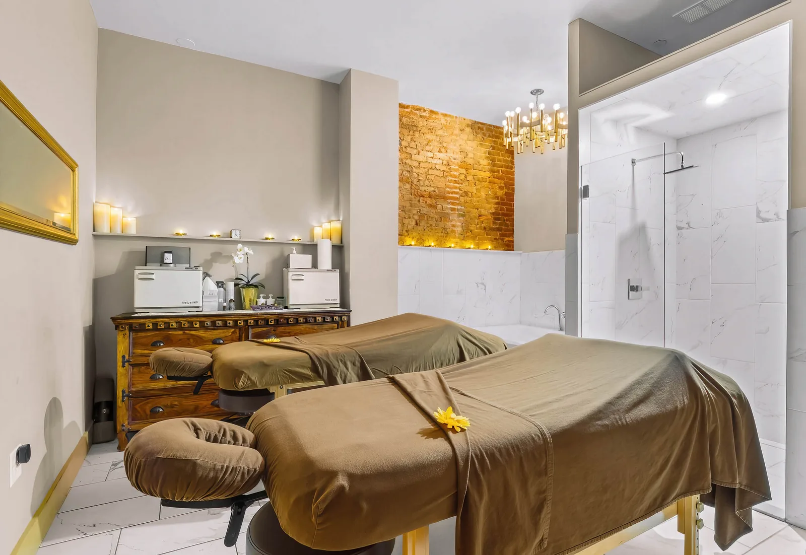 Cynergy spa couples massage room with two tables, exposed brick accent, candles, and marble shower, by OpenDoors360