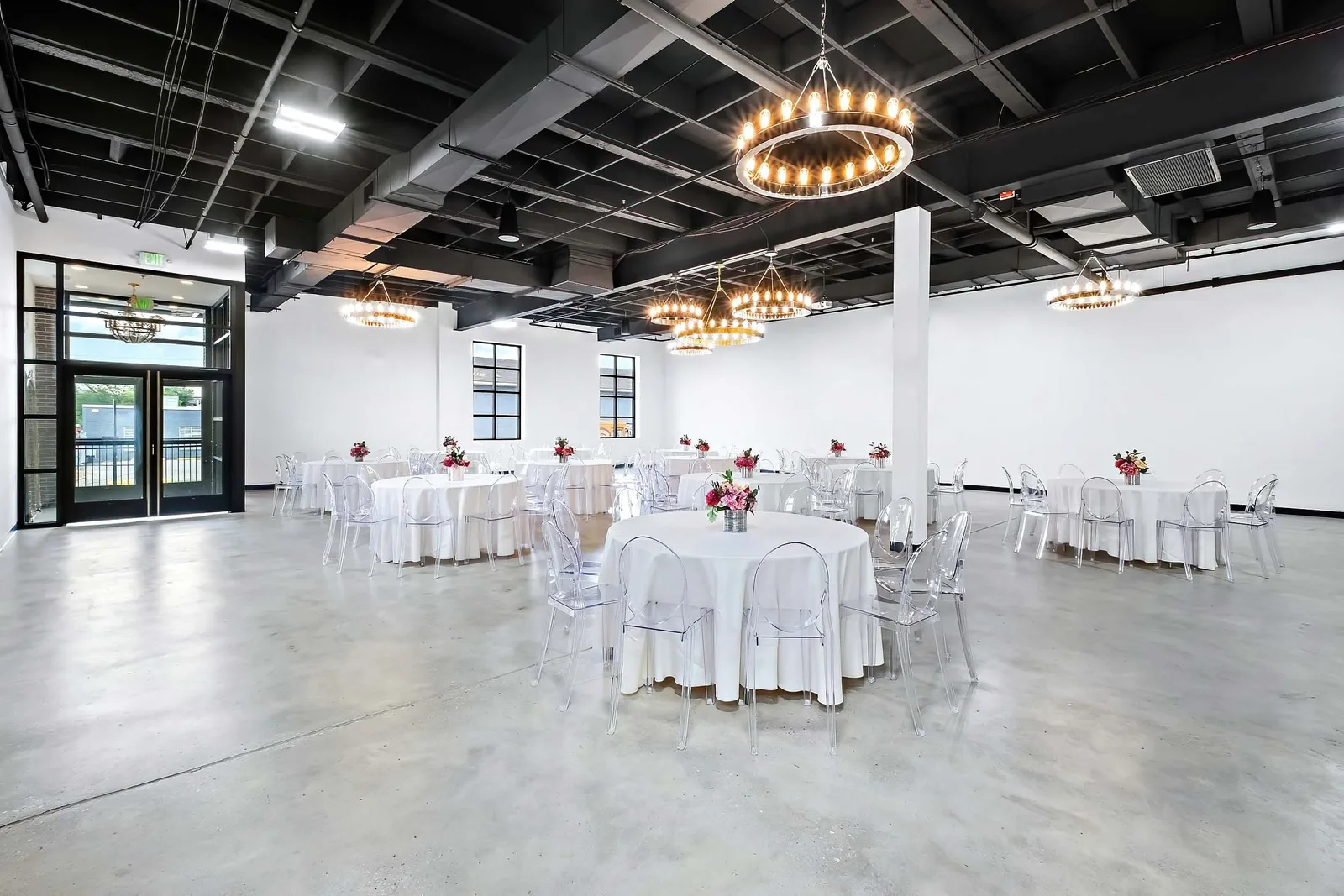 Event venue with round tables in white linens, ghost chairs, and circular chandeliers under black ceiling, by OpenDoors360