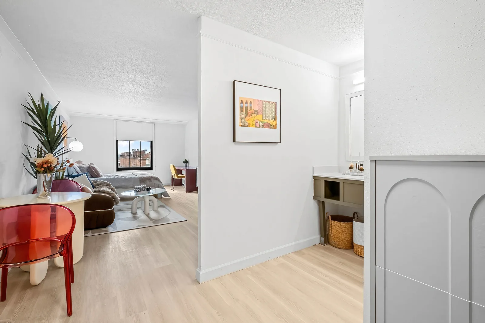 Studio apartment with staged living and sleeping area, framed art, and gray vanity near bright window, by OpenDoors360