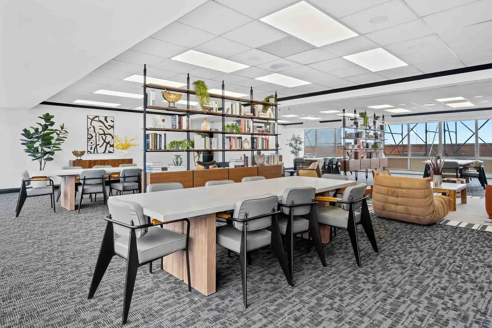 Co-working lounge with long shared table, bookshelf wall, and city windows, by OpenDoors360