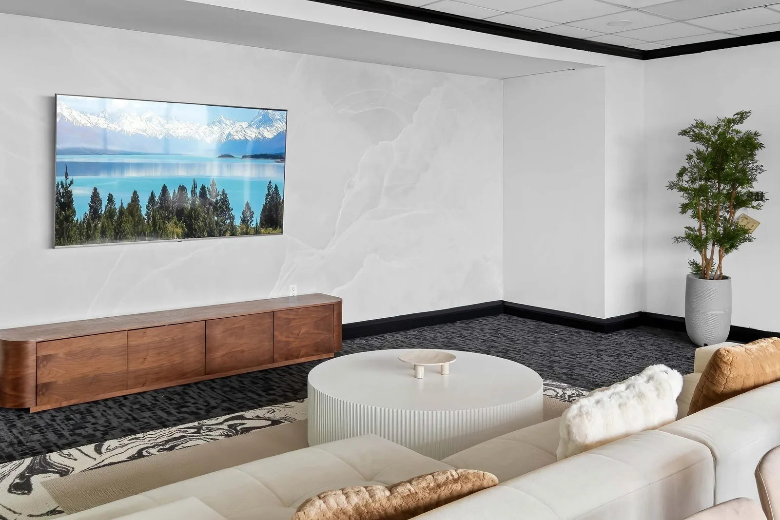 Media lounge with wall-mounted TV, round table, and dark carpet, by OpenDoors360
