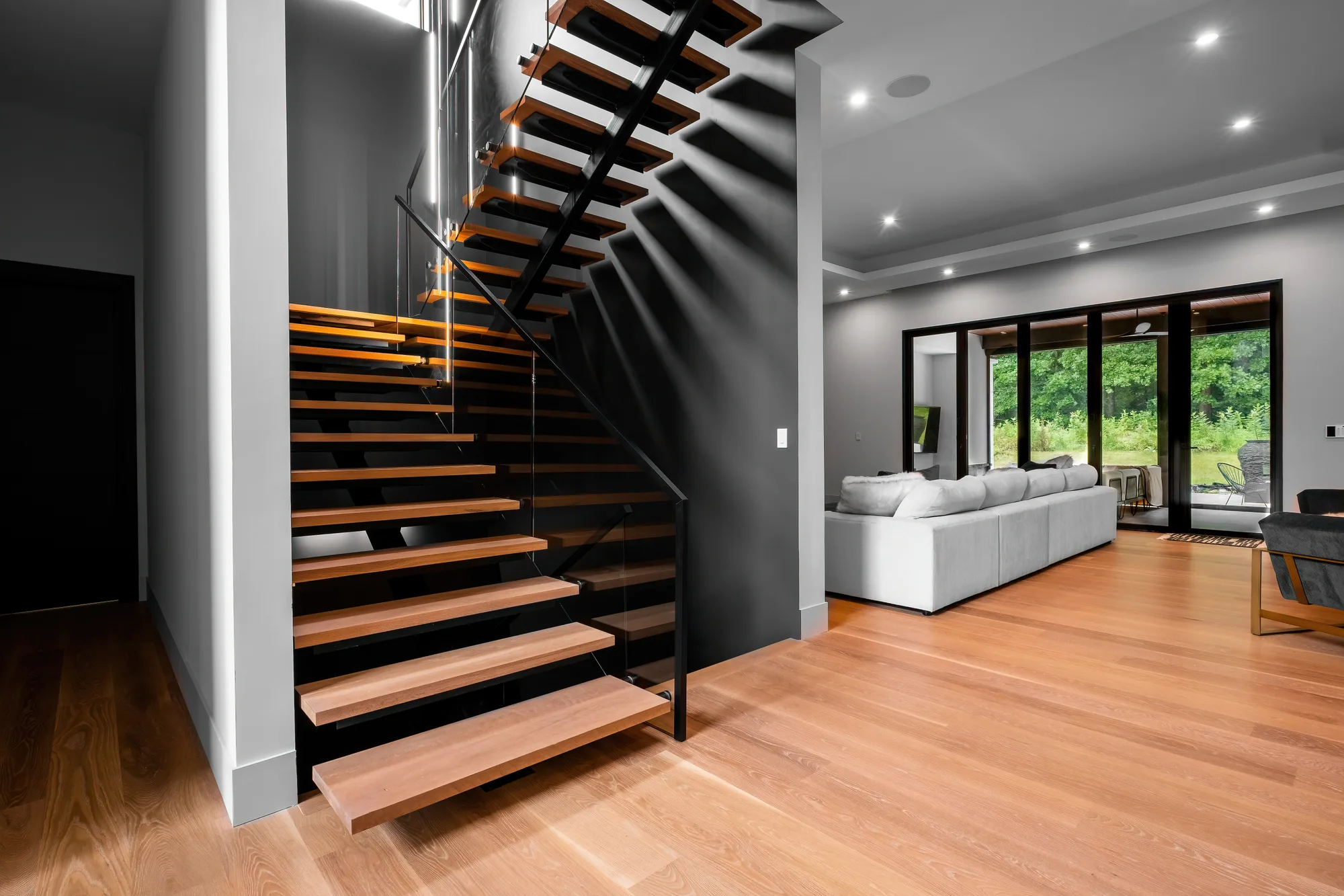 Floating wood staircase against black wall with open living room in Clifton, VA, by OpenDoors360