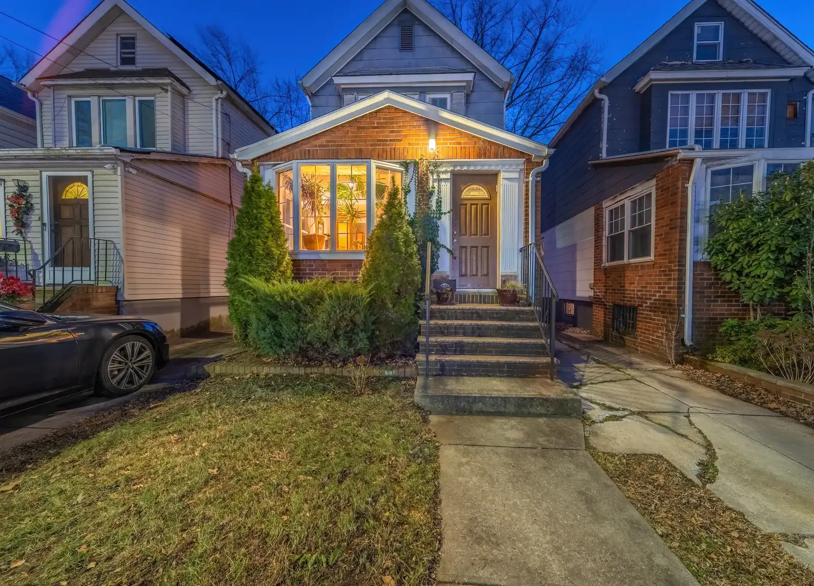 Queens single-family home exterior at twilight with lit front porch window, by OpenDoors360