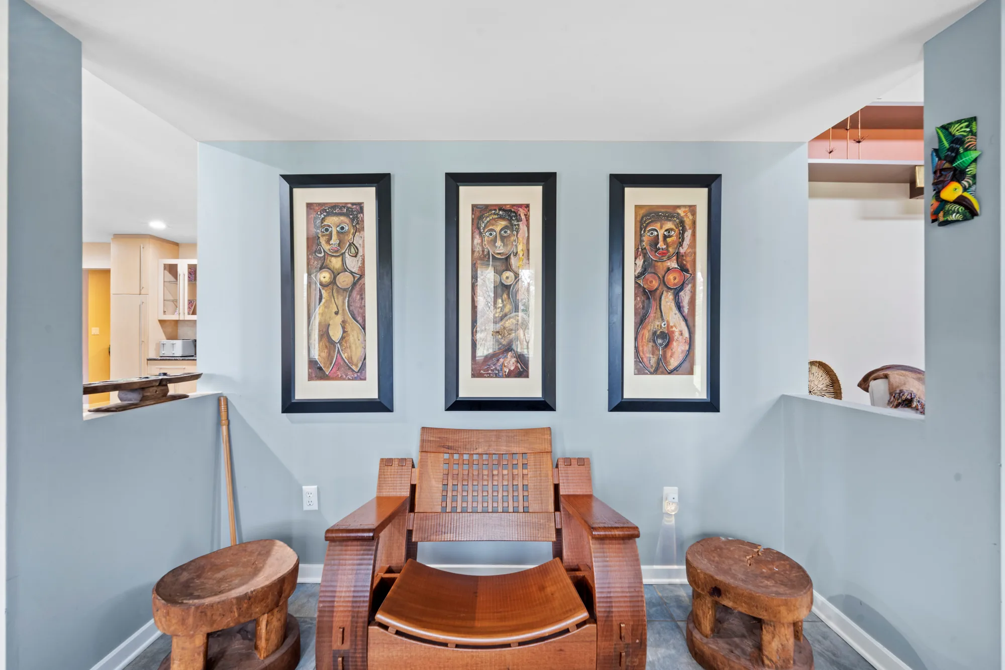 Blue-gray sitting nook with triptych of figural paintings and a carved wooden lounge chair, by OpenDoors360
